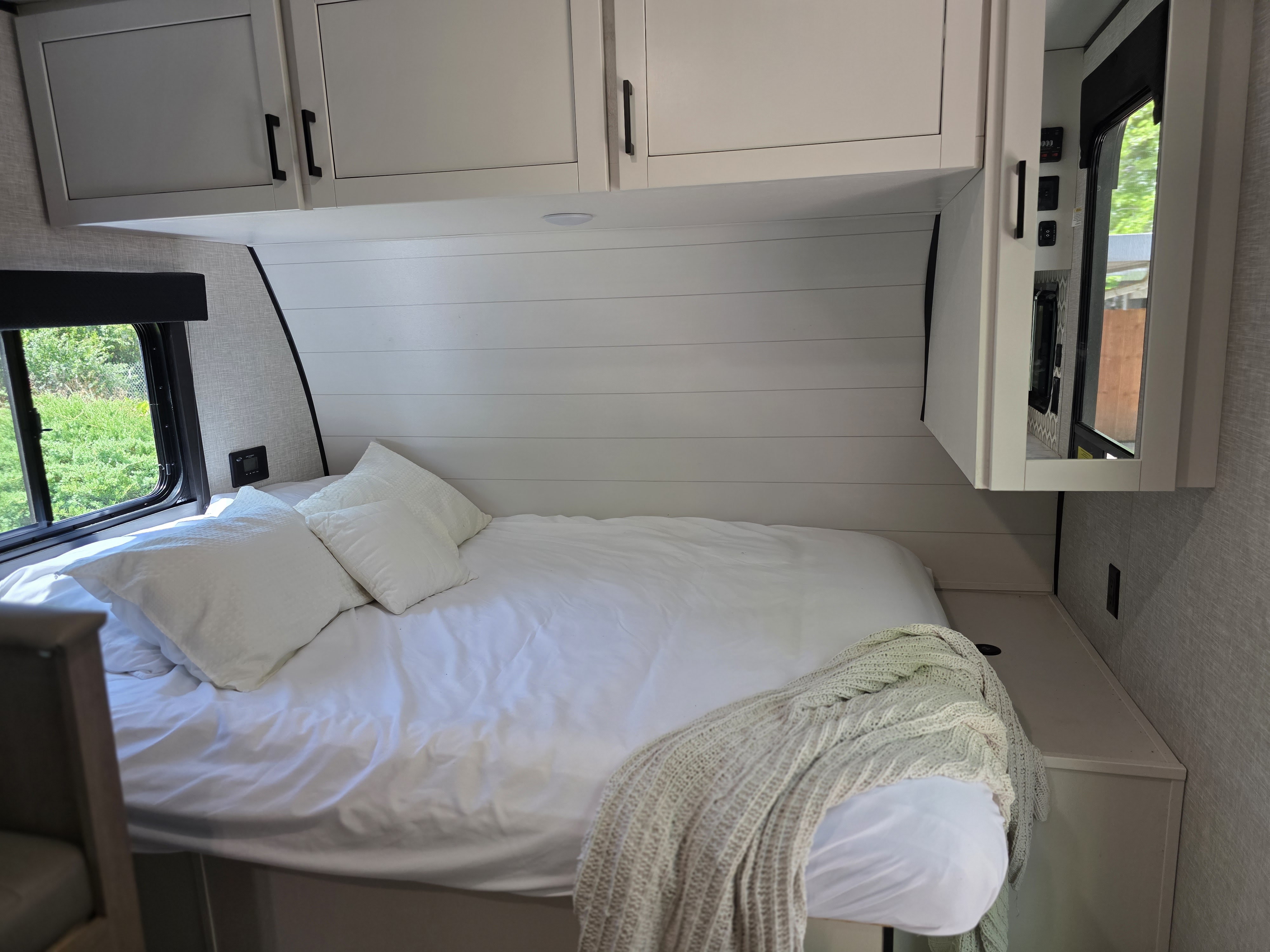 Modern RV rental bedroom featuring a comfortable bed, overhead cabinets, and a window with green views.. Highland Ridge Open Range MOAB 2025