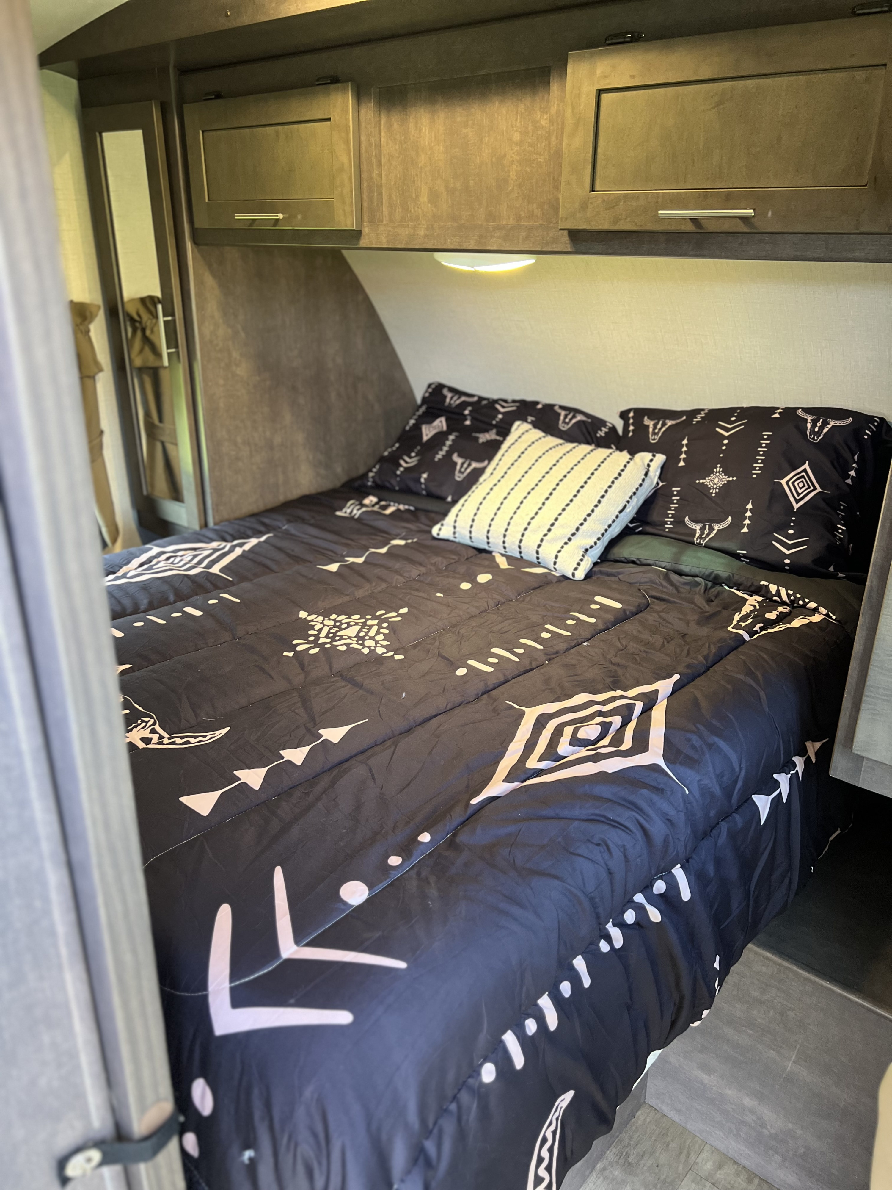 Cozy RV rental bedroom featuring patterned black and white bedding, a decorative pillow, and overhead cabinets.. Crossroads RV Sunset Trail Super Lite 2018