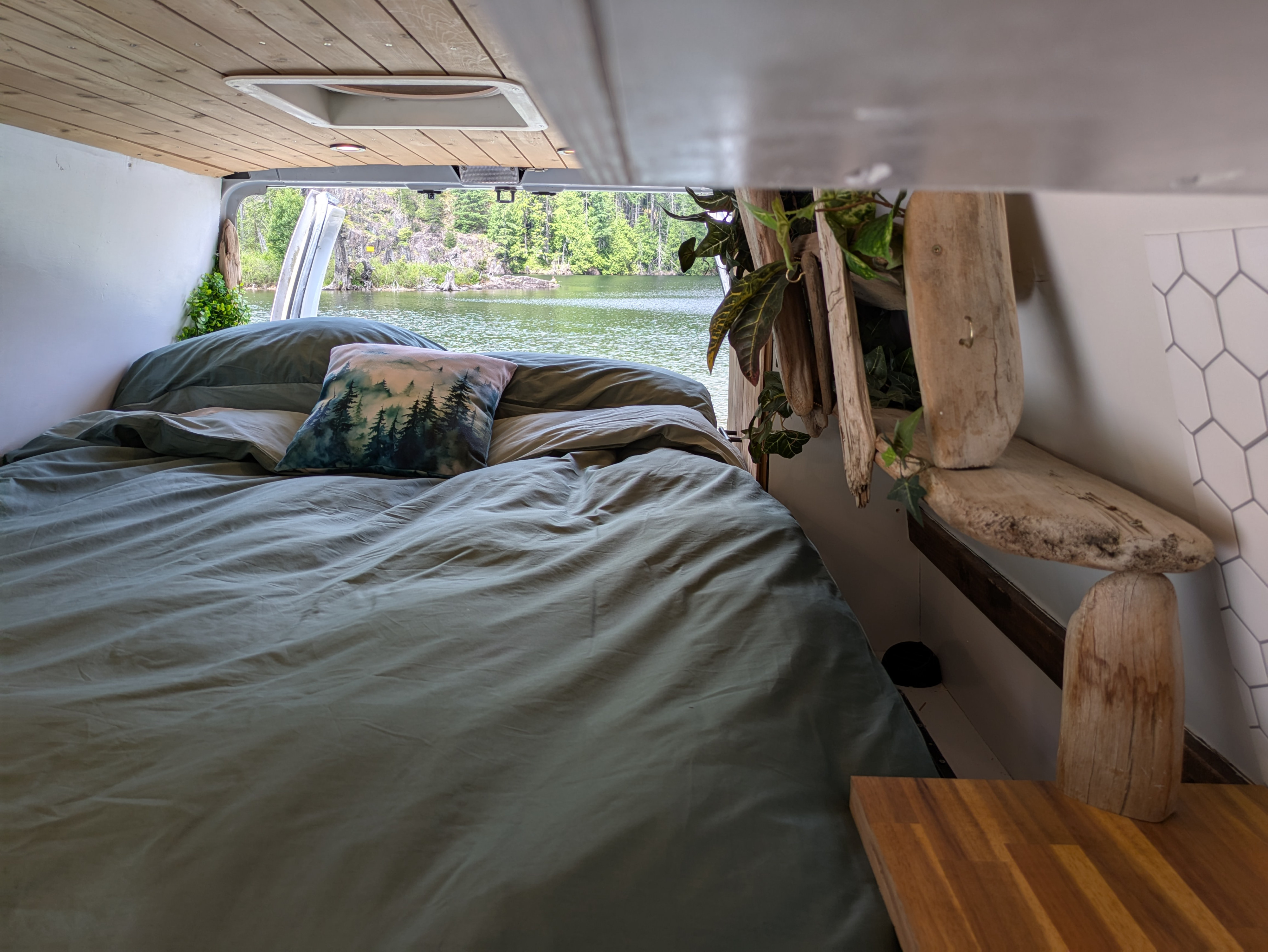 Inside an RV rental: a cozy bed overlooks a calm lake and lush forest, ideal for serene travel & van life.. Ford Econoline 2006