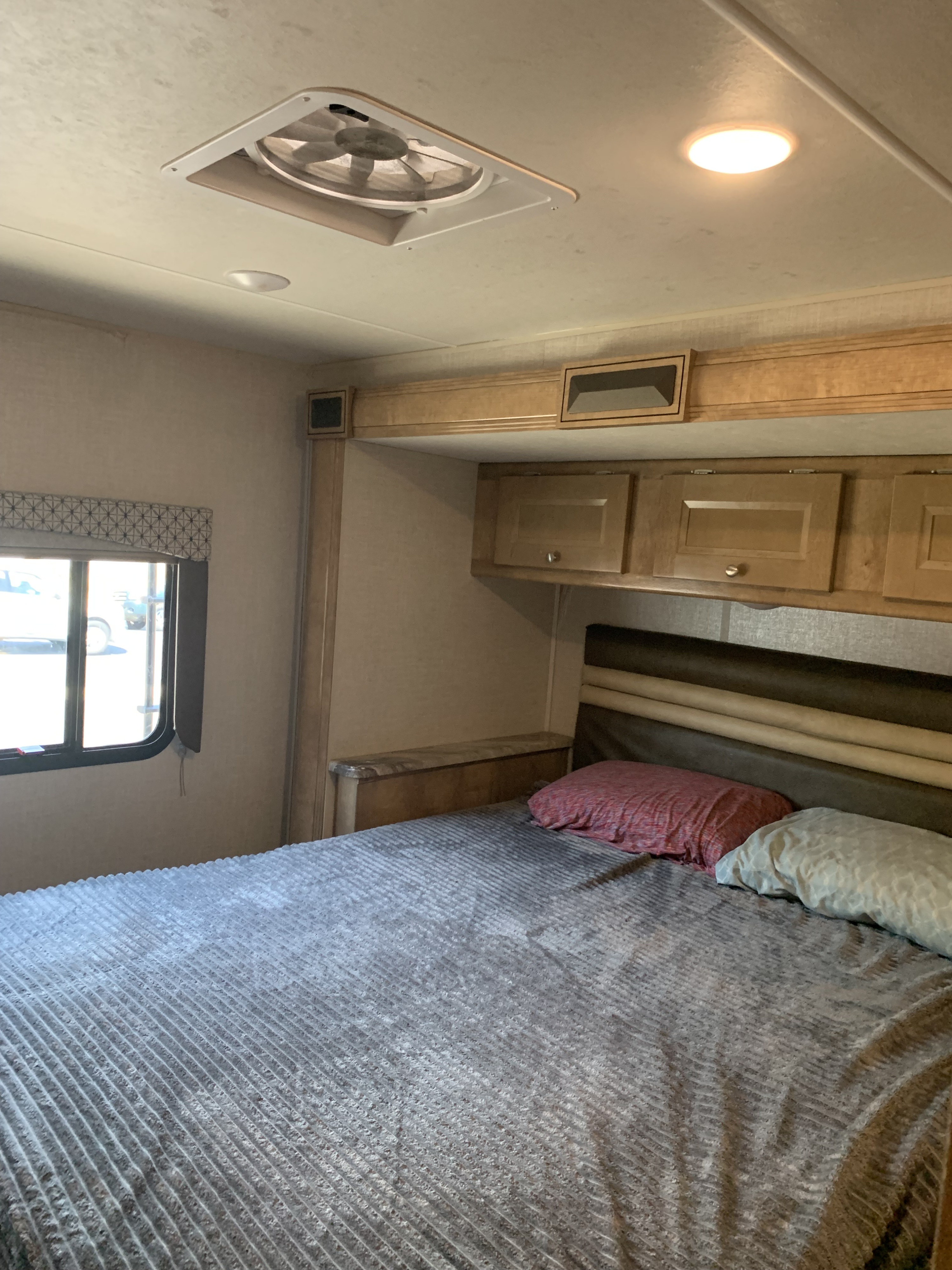 RV rental bedroom interior: A cozy bed with pillows, overhead cabinets, window, and a ceiling fan.. Forest River Coachmen Leprechaun 2020