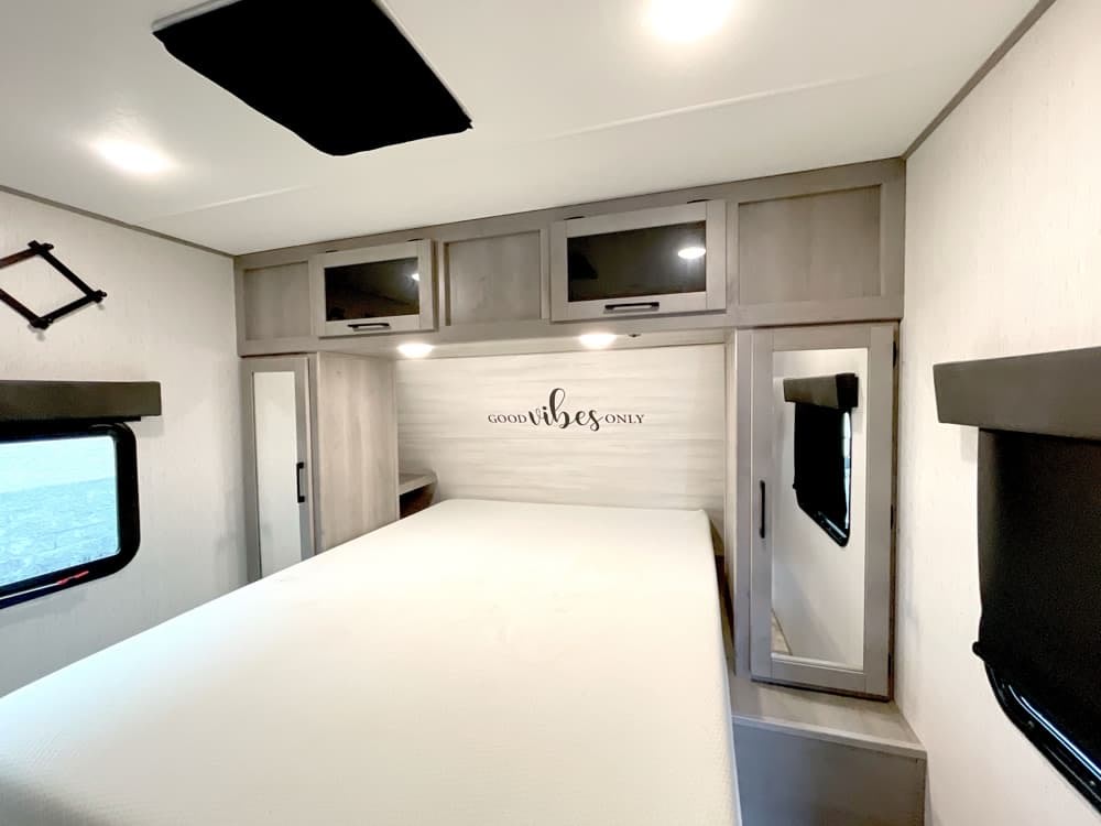 Comfortable RV rental bedroom: white bed, overhead cabinets, side wardrobes, and windows with shades.. Dutchmen Kodiak Ultra Lite 2022