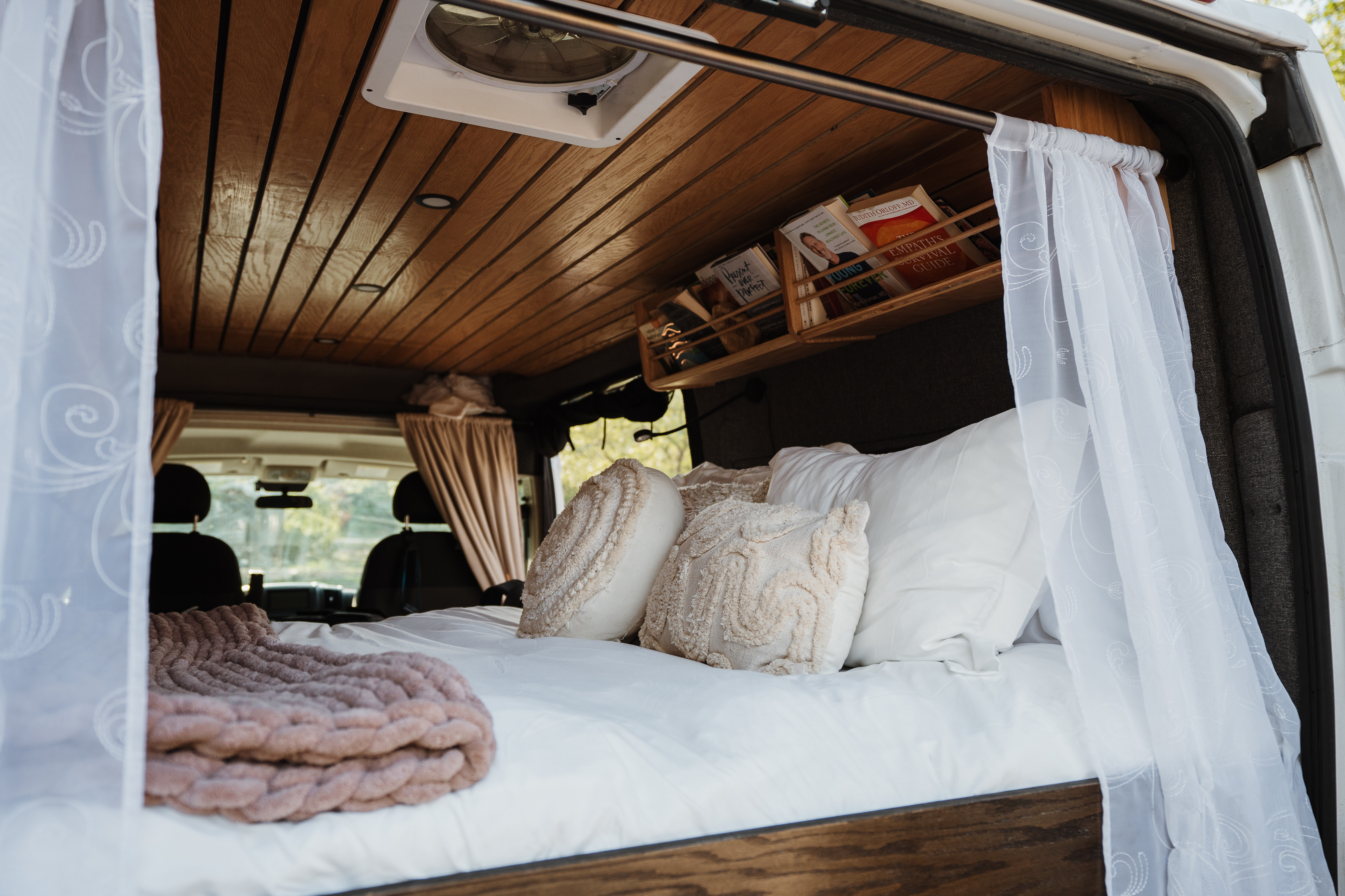 An rv rental's inviting bedroom: plush bed, decorative pillows, wood-paneled ceiling, and book storage.. Dodge 1500 2020