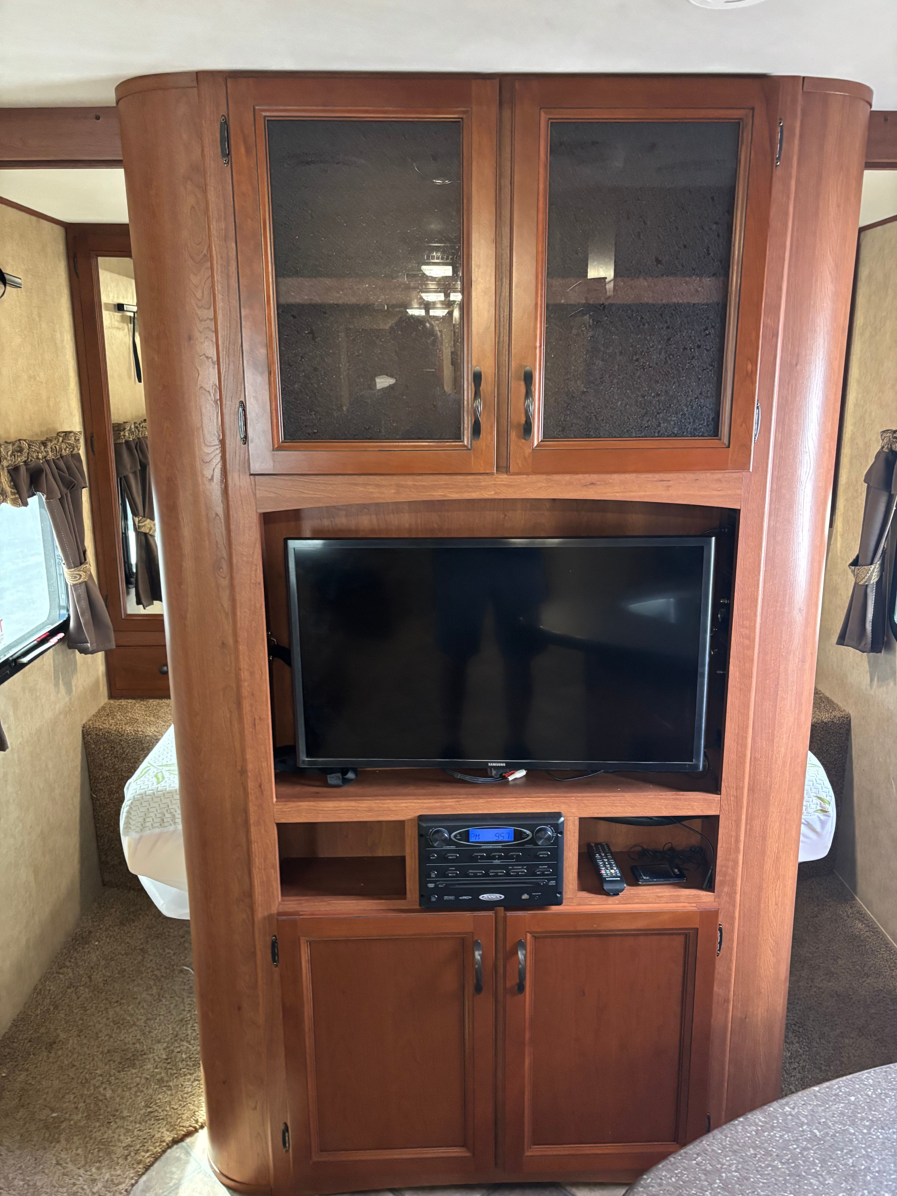Inside an RV rental: a wooden entertainment unit with TV and stereo, flanked by two bed areas.. Denali Denali Trailer 2013