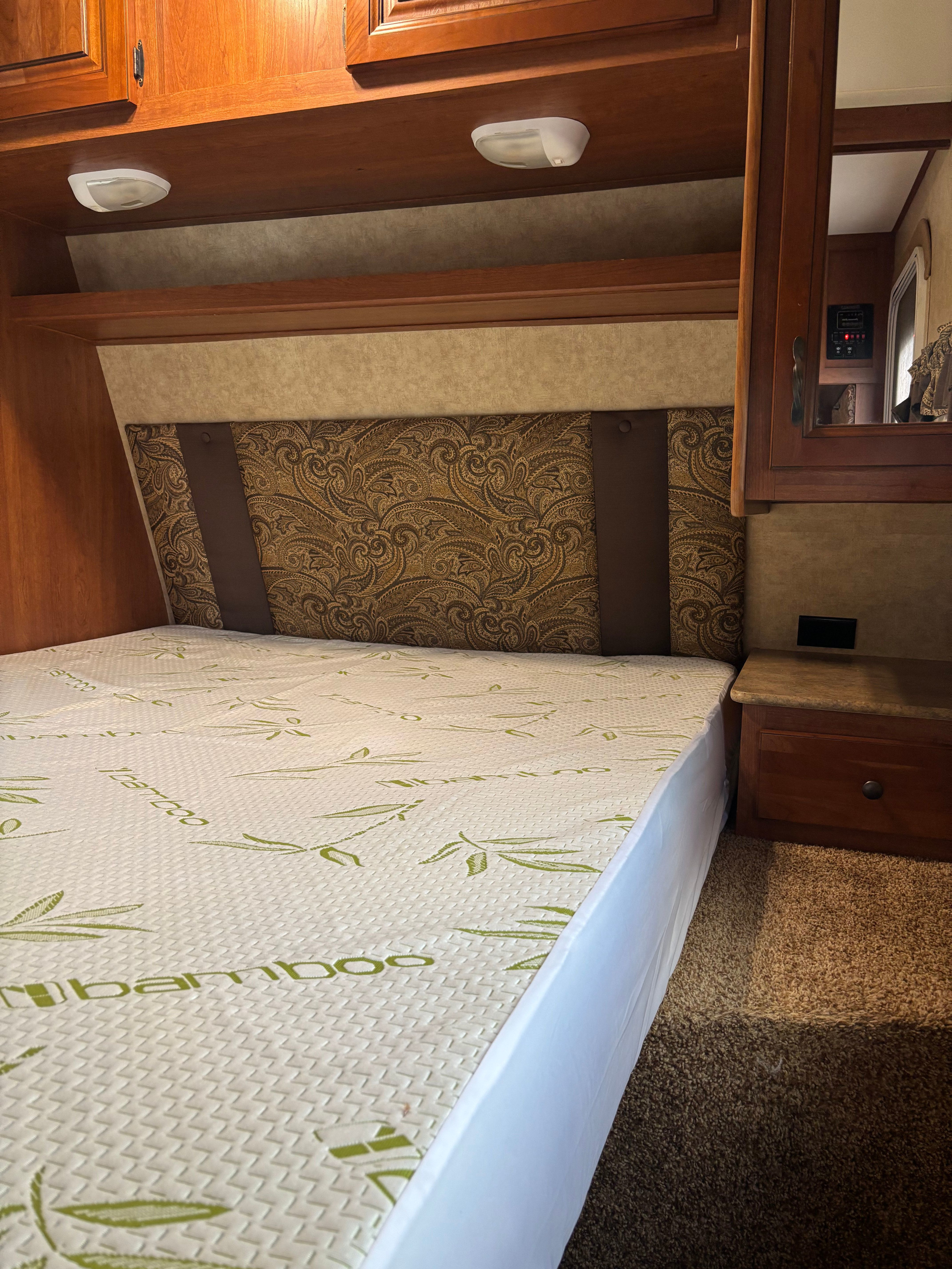 RV rental bedroom featuring a bed with a 'Bamboo' mattress, patterned headboard, wooden cabinets, and nightstand.. Denali Denali Trailer 2013
