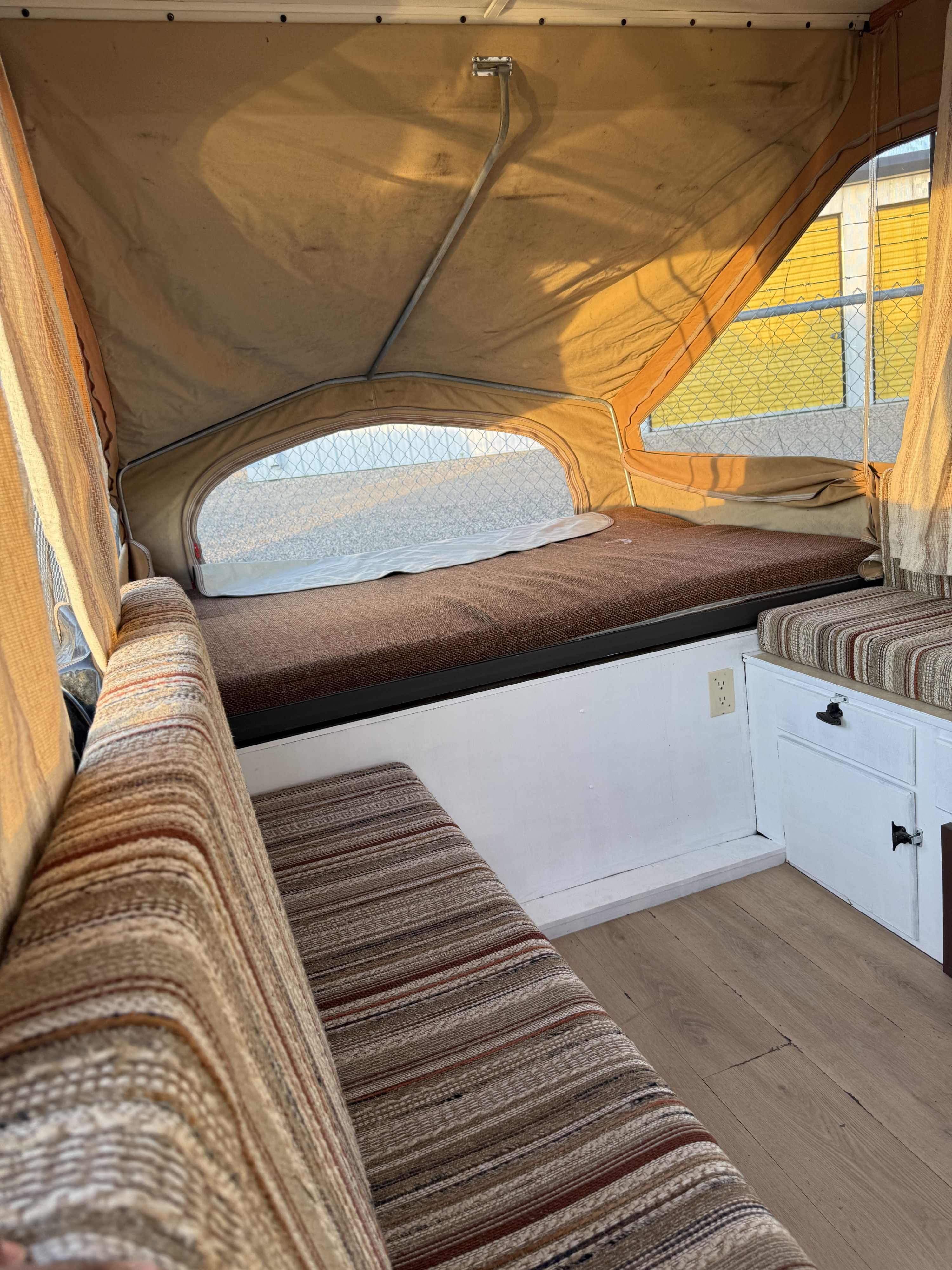 Pop-up camper RV rental interior features a cozy bed, striped bench seating, and wood-look flooring.. Jayco Jay Series 1984