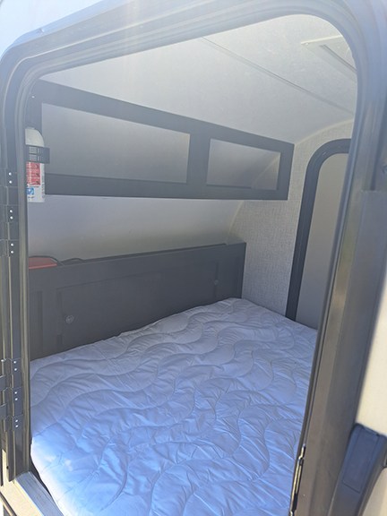 Cozy RV rental interior with a bed, overhead storage, and a fire extinguisher. Perfect for camping!. Braxton Creek Bushwhacker 2021