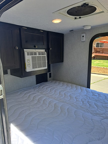 Cozy RV rental interior featuring a quilted mattress, wall-mounted AC, overhead cabinets, and a ceiling fan, ready for adventure.. Braxton Creek Bushwhacker 2021