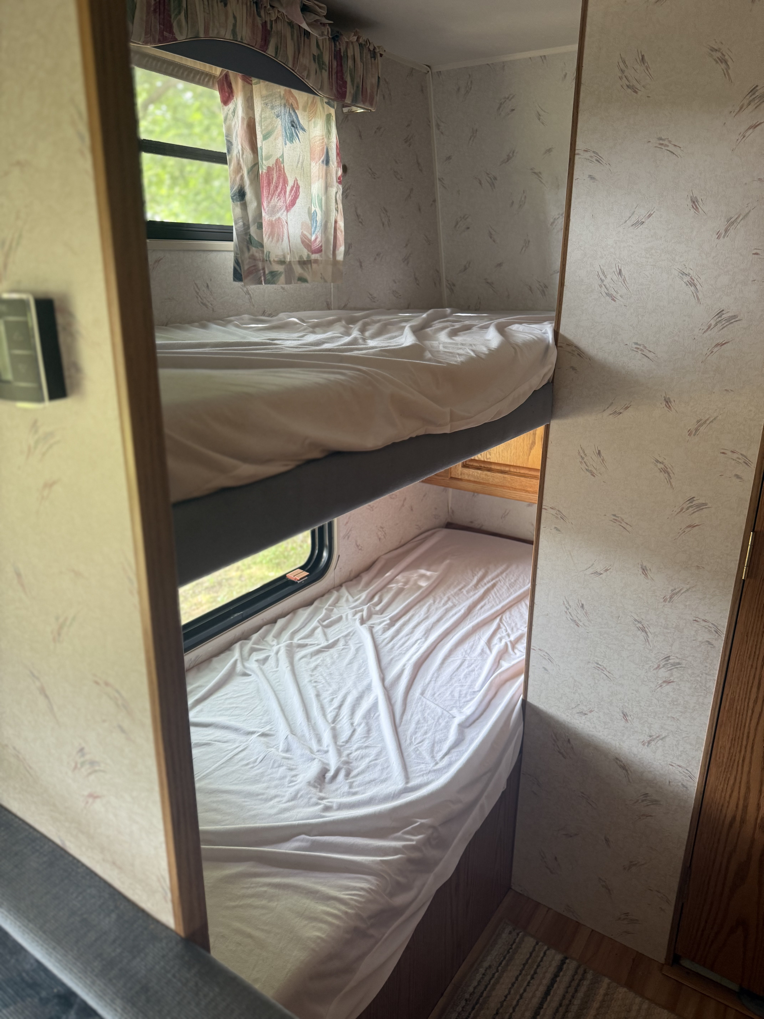 RV rental bunk beds with white sheets, a window with floral curtains, and patterned walls.. Jayco 300dbbh 1994