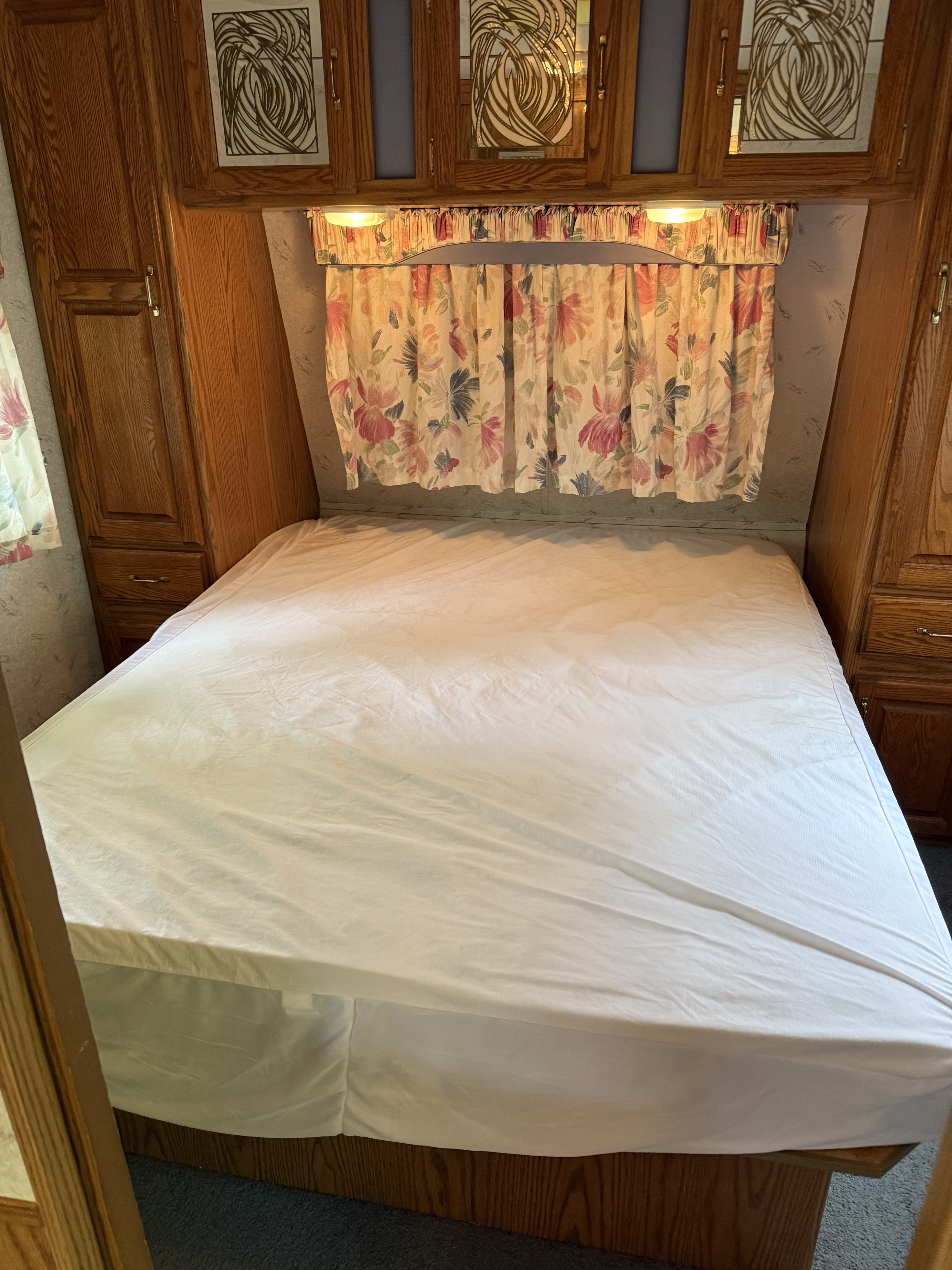 This RV rental's bedroom offers a comfortable bed, overhead cabinets, and charming floral window treatments.. Jayco 300dbbh 1994