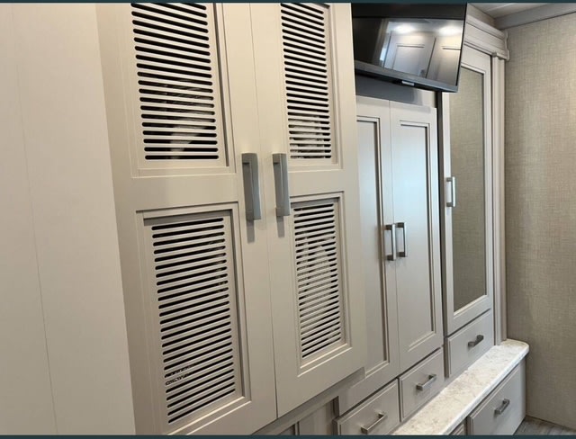 RV rental interior: Built-in cabinetry with louvered vents, a TV, and mirrored closet offer ample storage.. Thor Miramar 2023