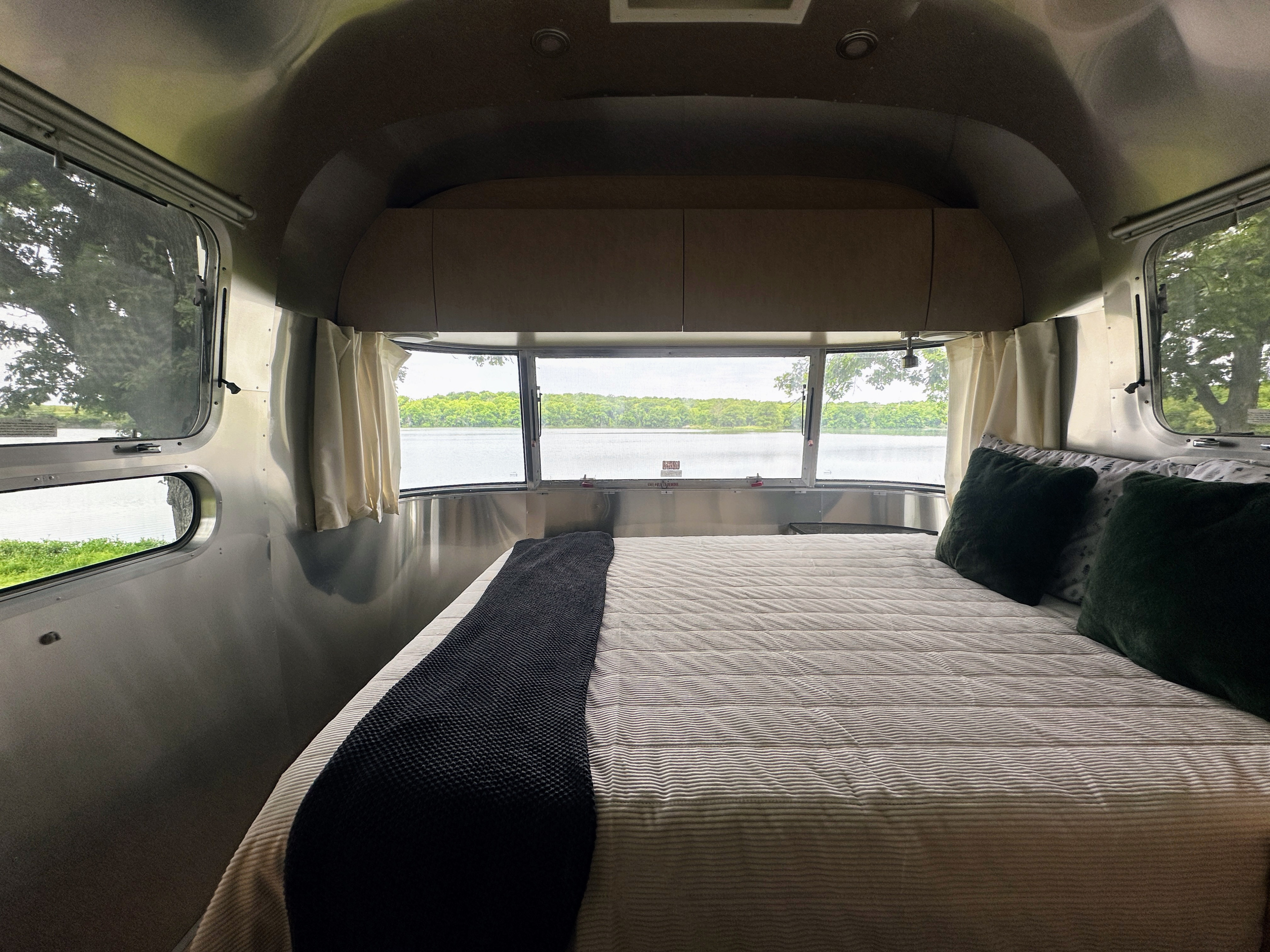 Serene lake views from the cozy bedroom of an Airstream RV rental. Perfect for a tranquil escape.. Airstream Flying Cloud 2012