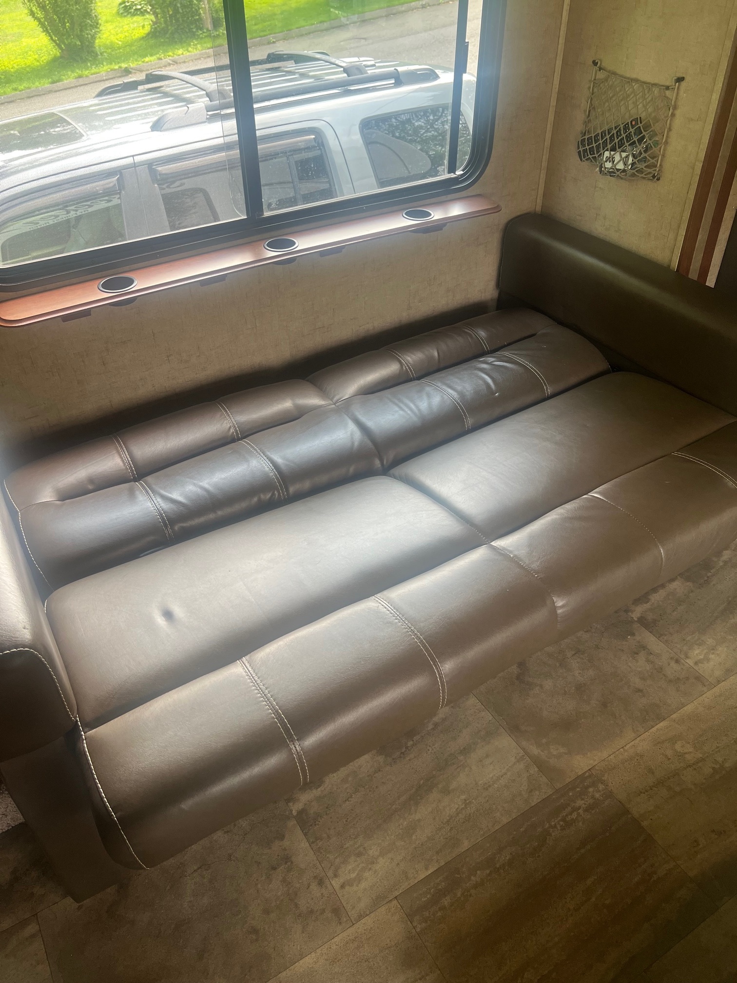 Comfy RV rental interior: brown convertible sofa, window view, cup holders, & wall storage. Ready for adventure!. Forest River Sunseeker 2016