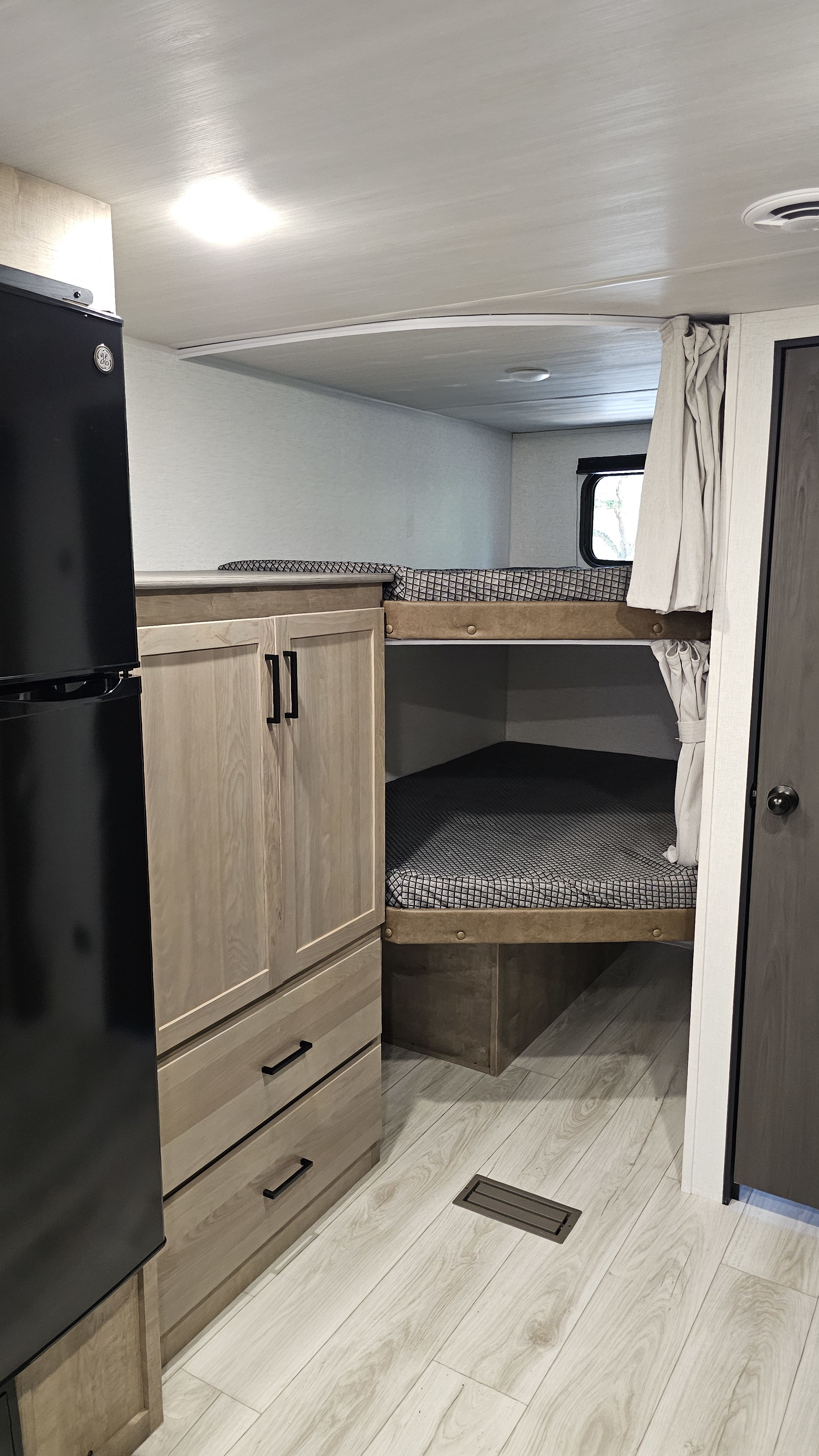 Inside a cozy RV rental: light wood bunk beds, integrated storage cabinet, and fridge, visible on light flooring.. Keystone RV Springdale 2025