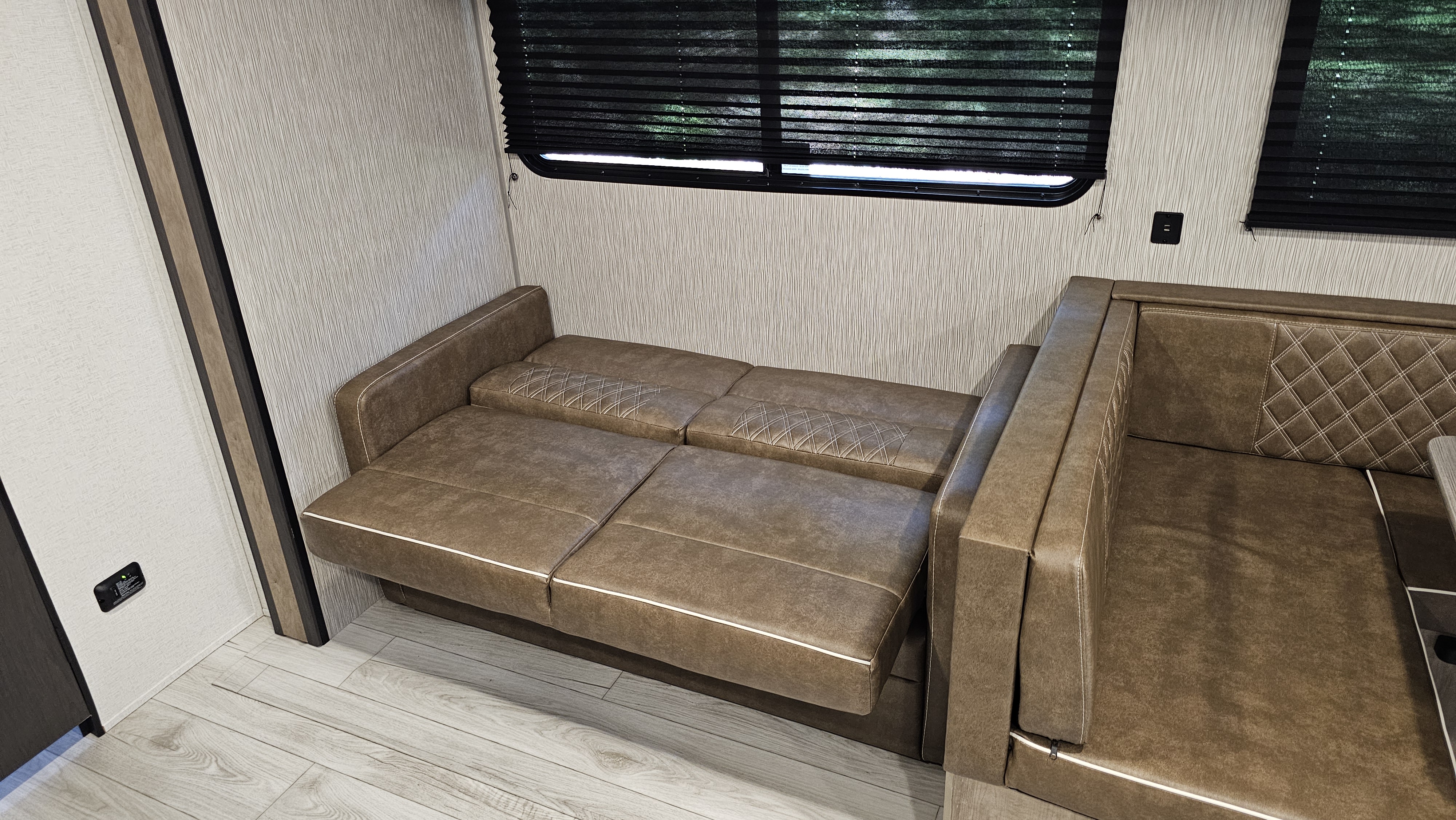 Inside your RV rental: a modern brown sofa bed and dinette, offering flexible living and sleeping space.. Keystone RV Springdale 2025