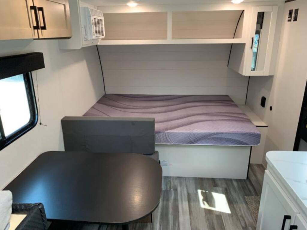 RV rental interior: A comfortable bed with a patterned mattress, a dinette with a dark table, and white overhead cabinets.. Jayco Jay Flight 2026