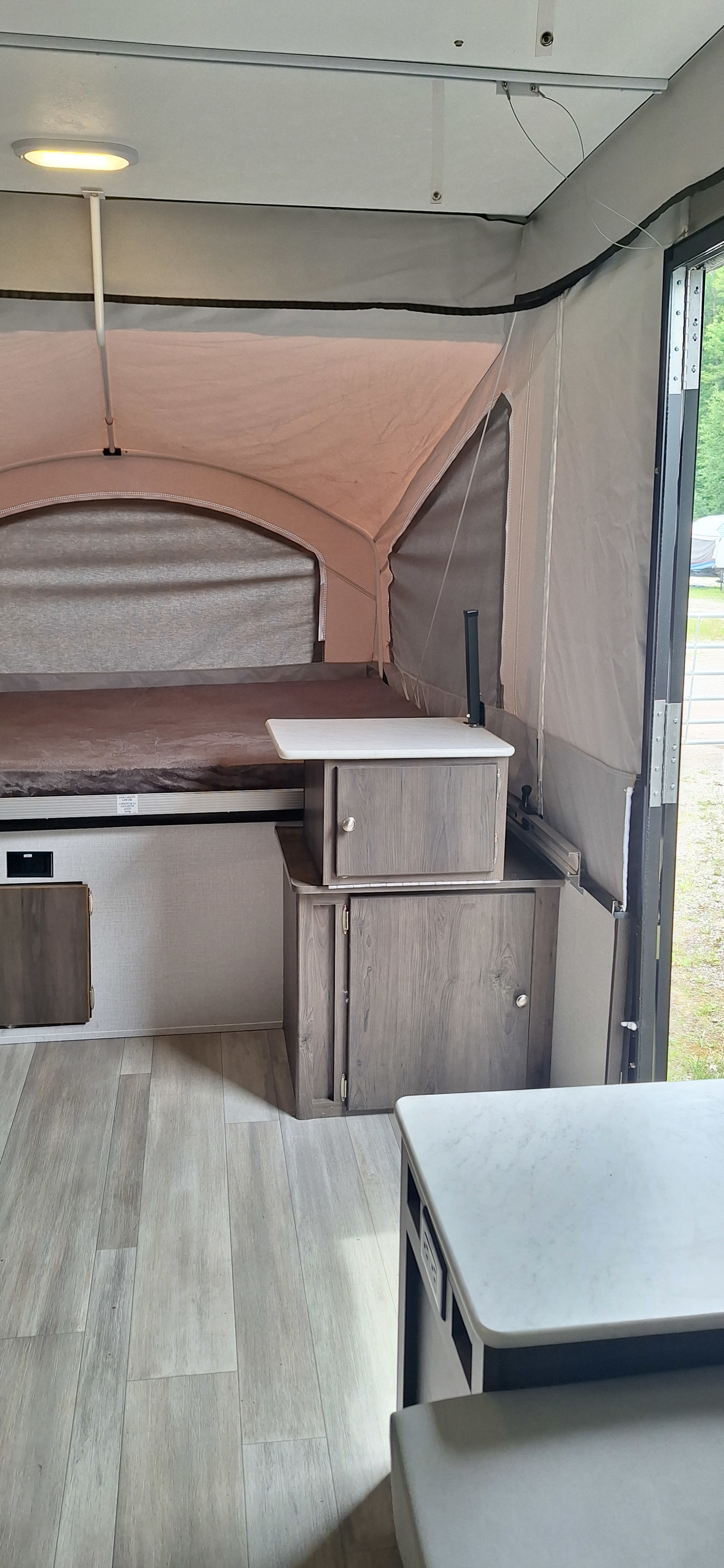 This RV rental interior features light wood floors, a cozy pop-out bed, compact cabinets, and a counter, ready for camping.. Forest River Viking 2022