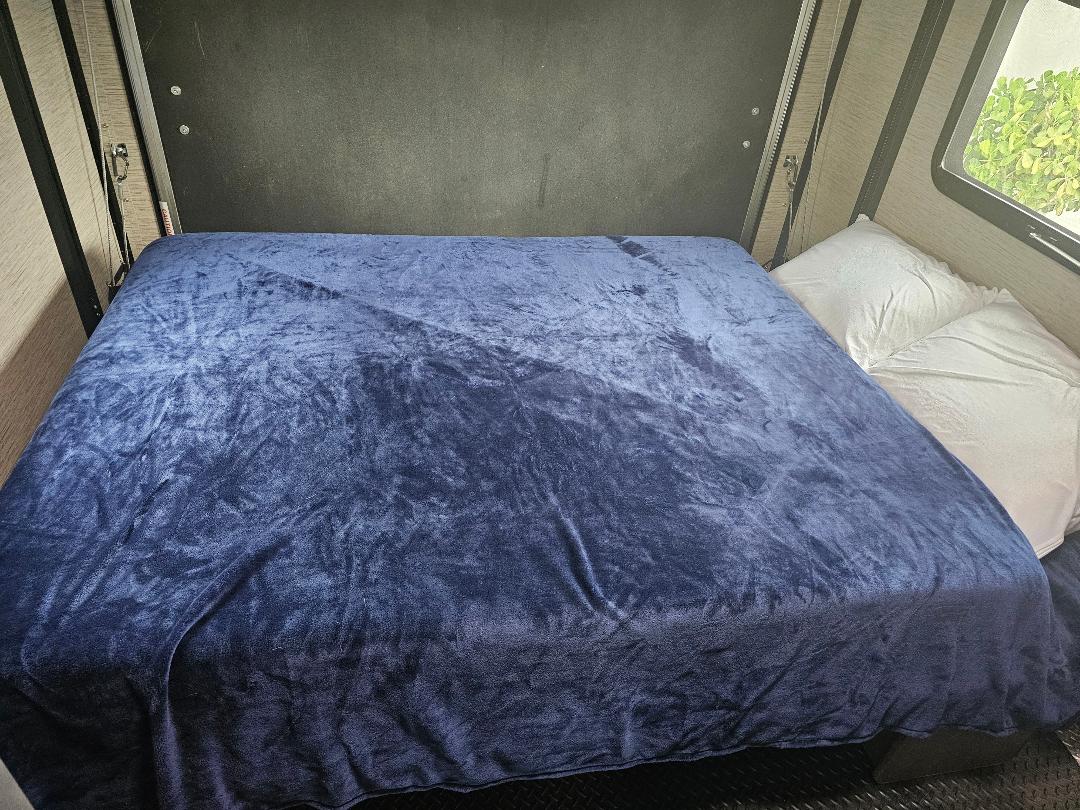 RV rental: A comfy bed with a plush blue blanket and white pillows, ready for restful nights on your travels.. Thor Outlaw 2021