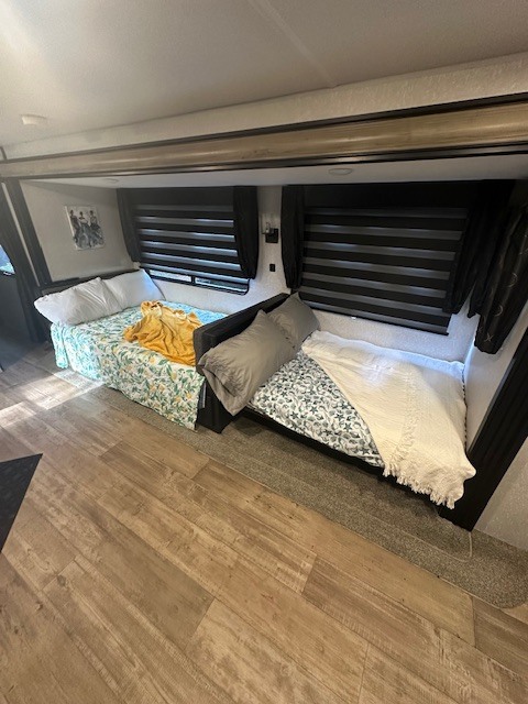Cozy RV rental interior with two beds, wood-look flooring, and windows with dark horizontal blinds.. Forest River Cherokee 2022