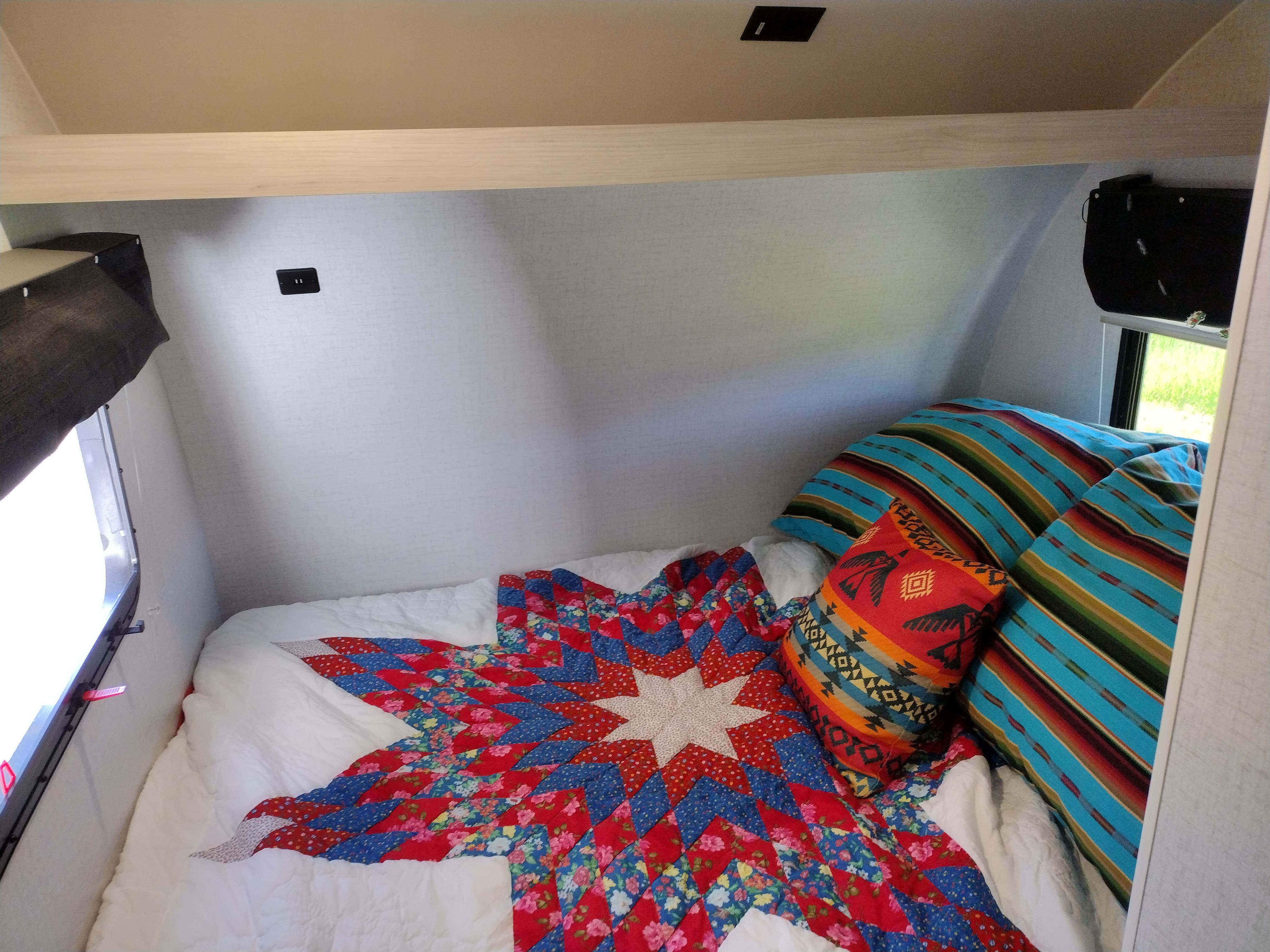 Comfortable RV rental sleeping area with a vibrant star quilt, colorful patterned pillows, and bright windows.. Winnebago Hike 2022