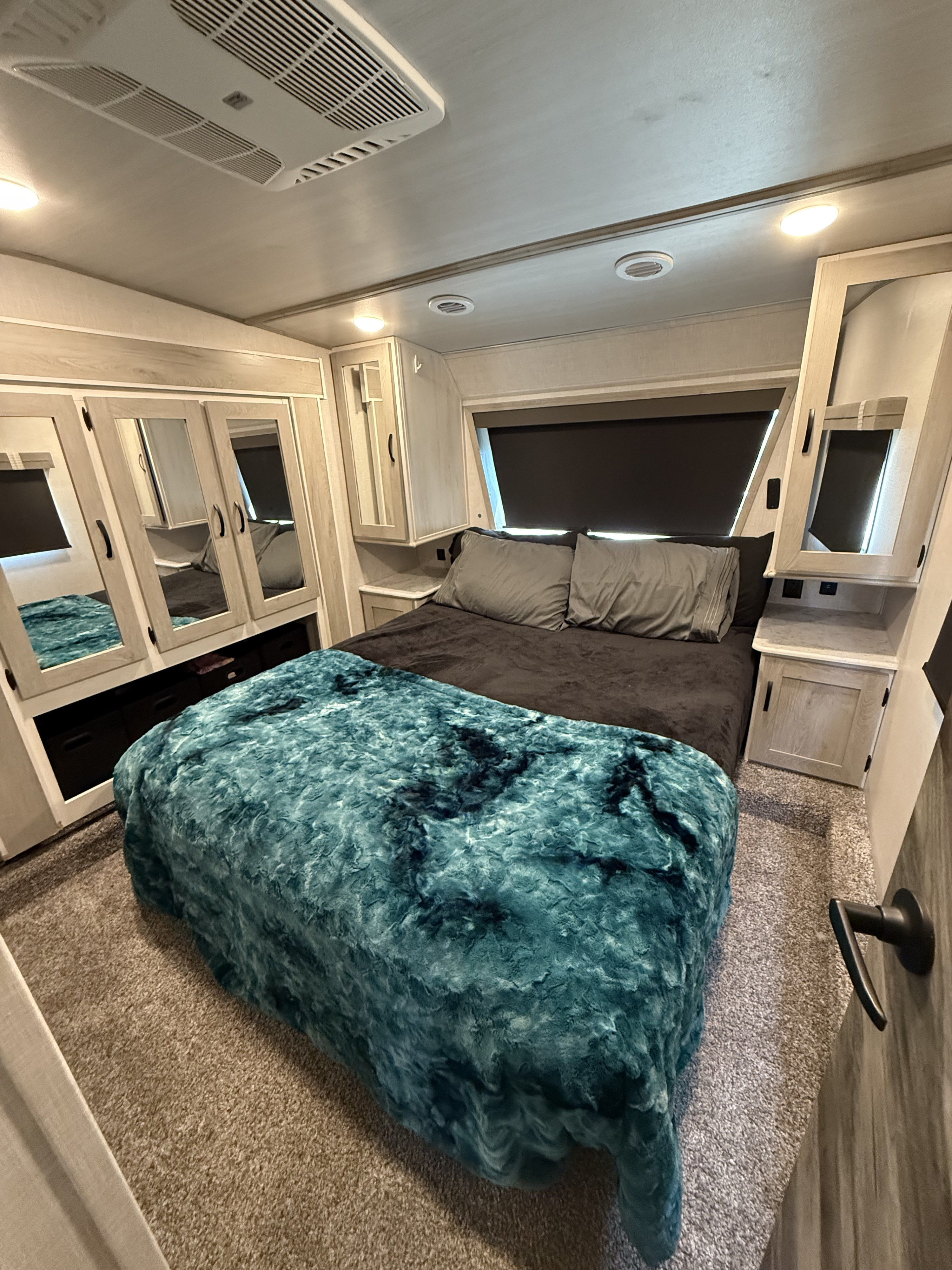 Cozy RV rental bedroom with built-in mirrored storage, a comfortable bed, and a plush teal blanket.. Forest River Impression 2022