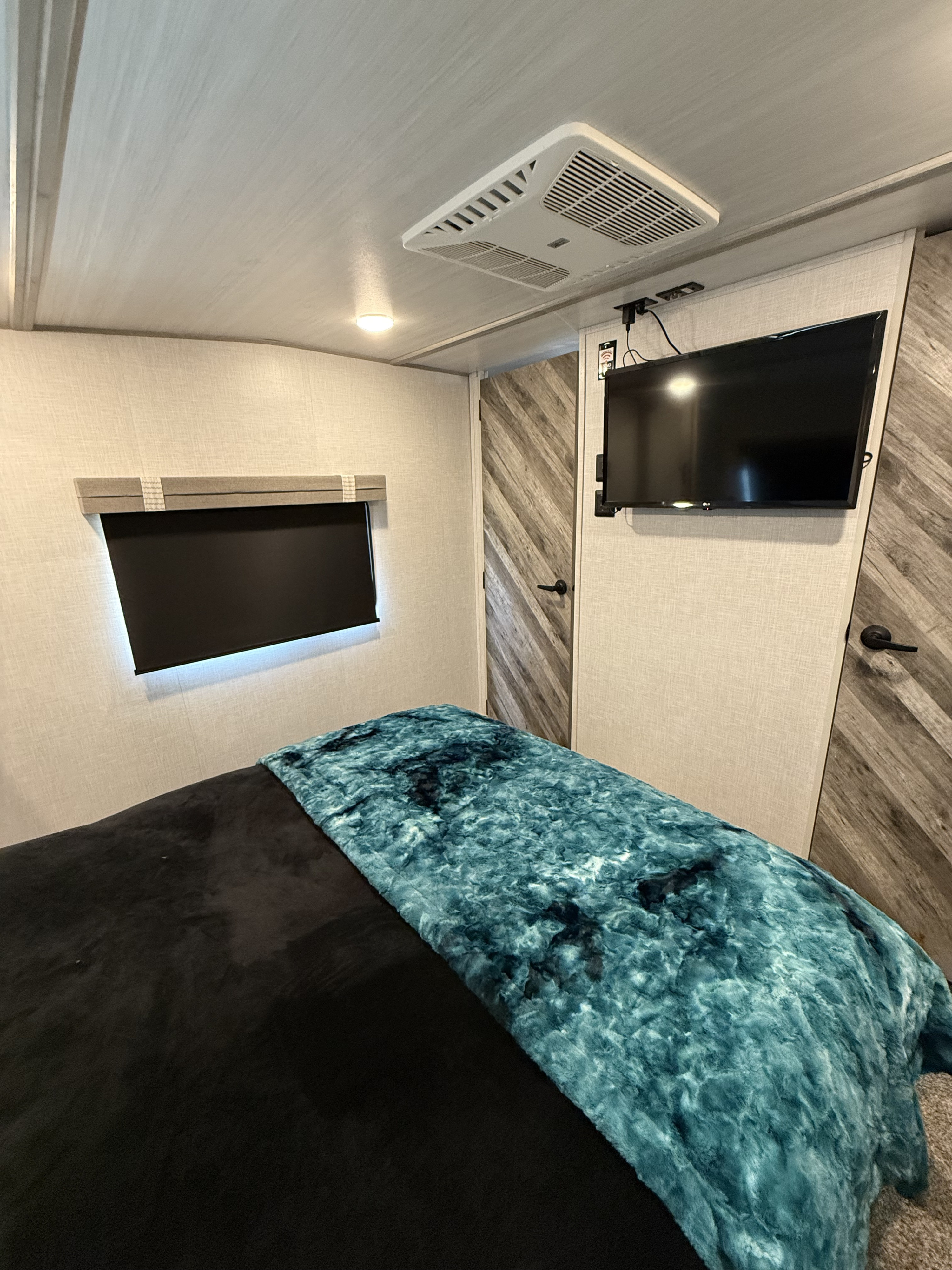 Cozy RV bedroom interior with a teal blanket, window, TV, and AC unit. Perfect for your next RV rental adventure.. Forest River Impression 2022
