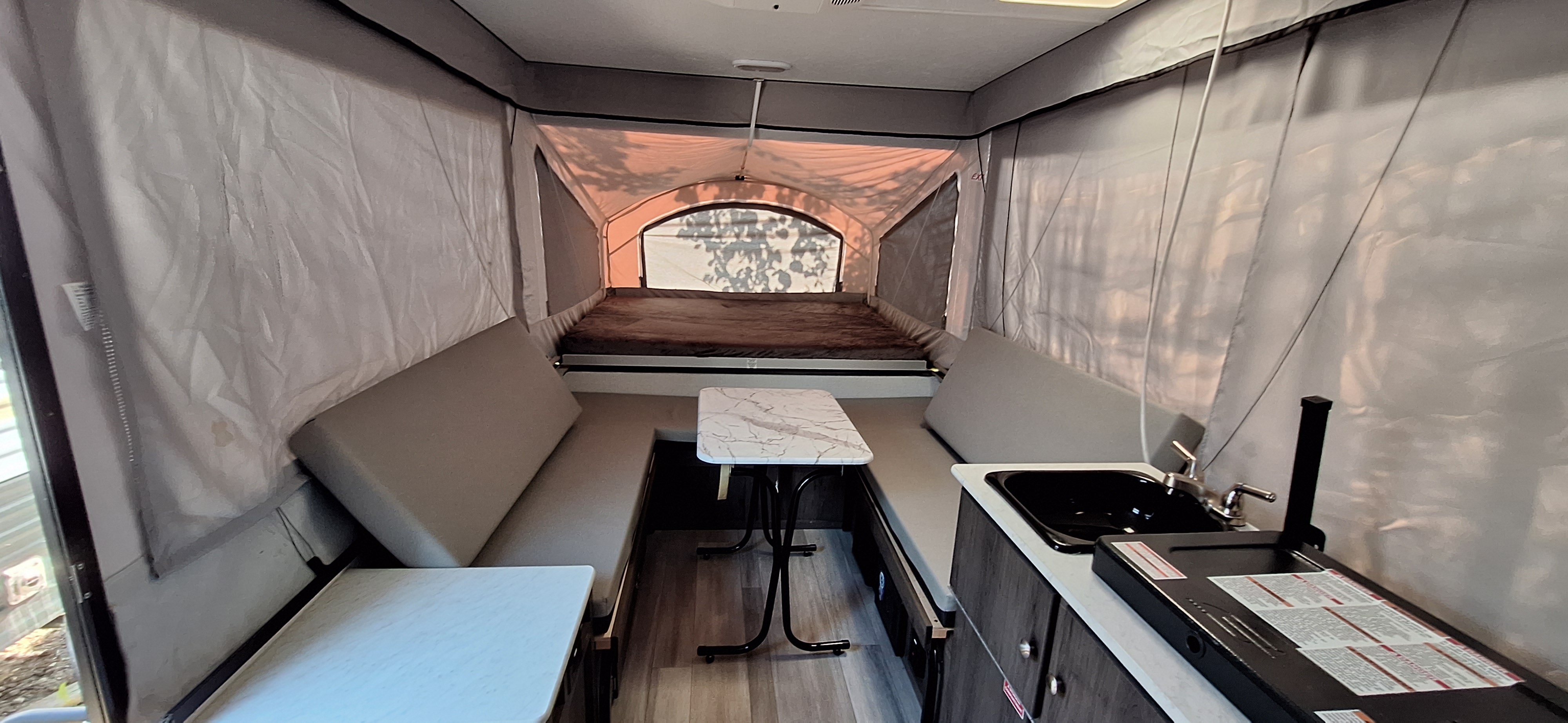 Interior of a pop-up RV rental, featuring the bed, seating, dining table, and kitchenette with sink.. Forest River Viking 2022
