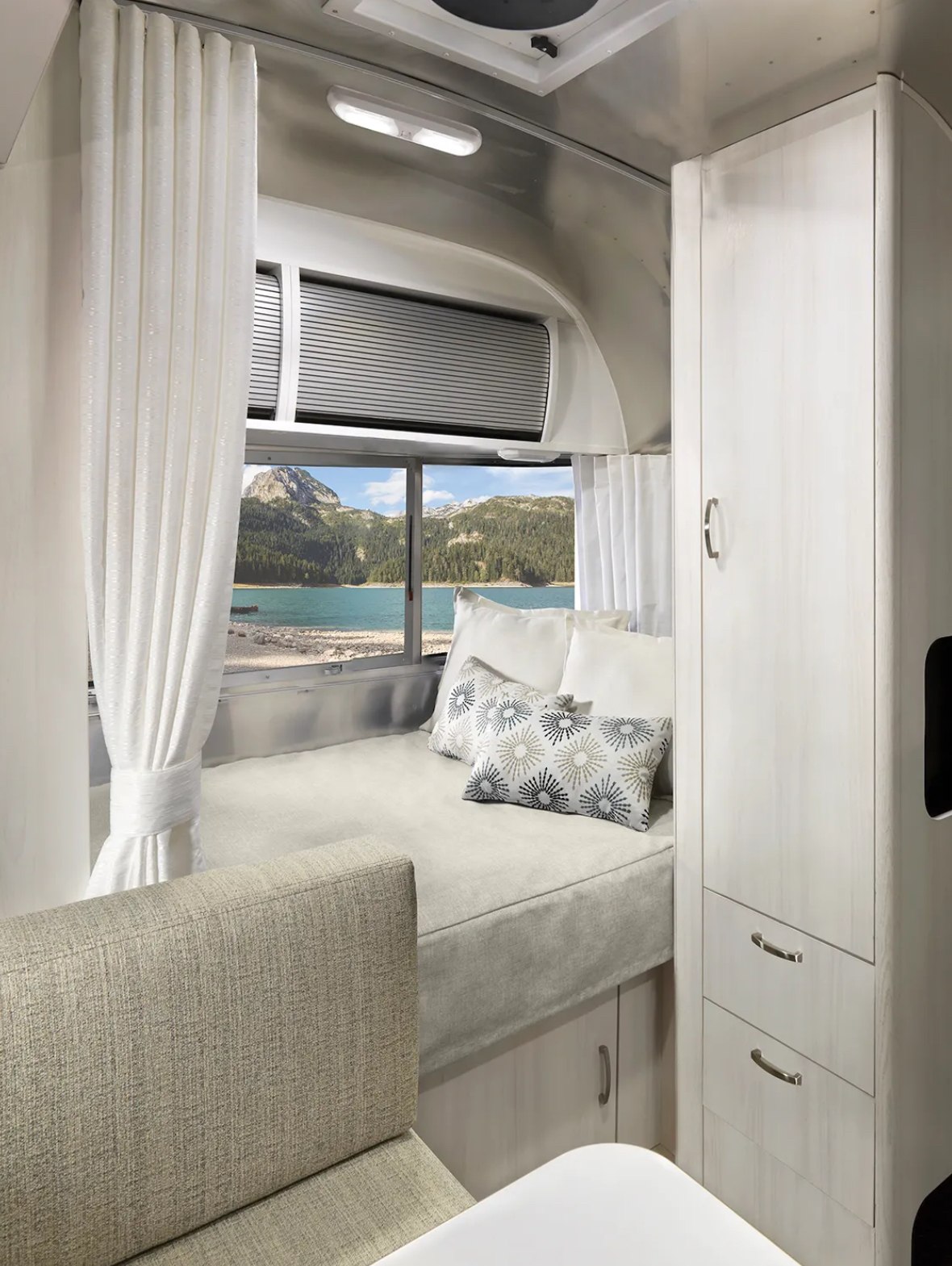 Cozy RV rental interior with bed, cabinets, and stunning lake/mountain views through the window. Perfect for your next adventure.. Airstream Airstream 2025
