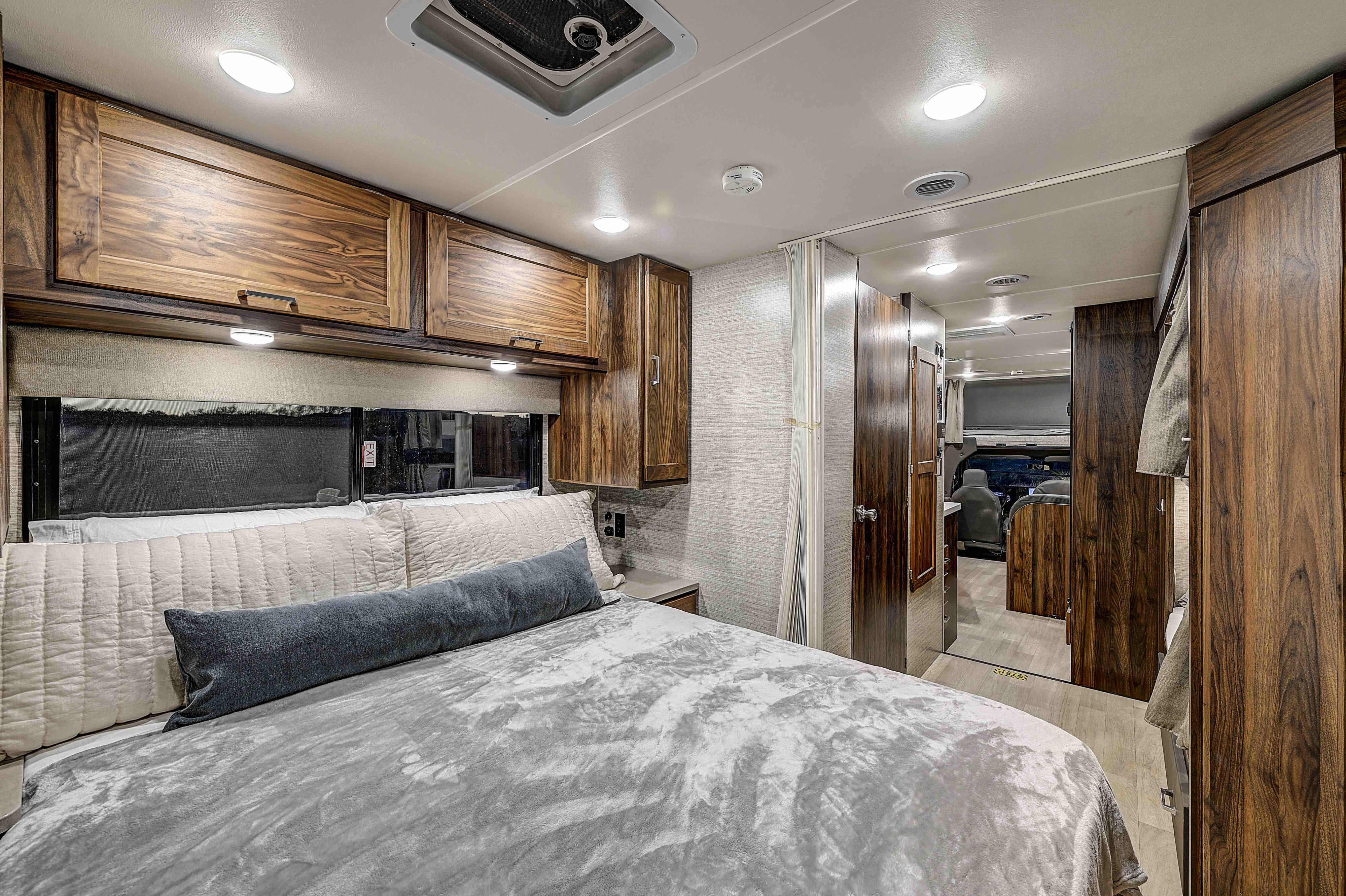 Cozy rv rental bedroom: A comfortable bed, warm wooden cabinetry, and bright lighting provide a welcoming motorhome interior.. Winnebago Minnie Winnie 2023