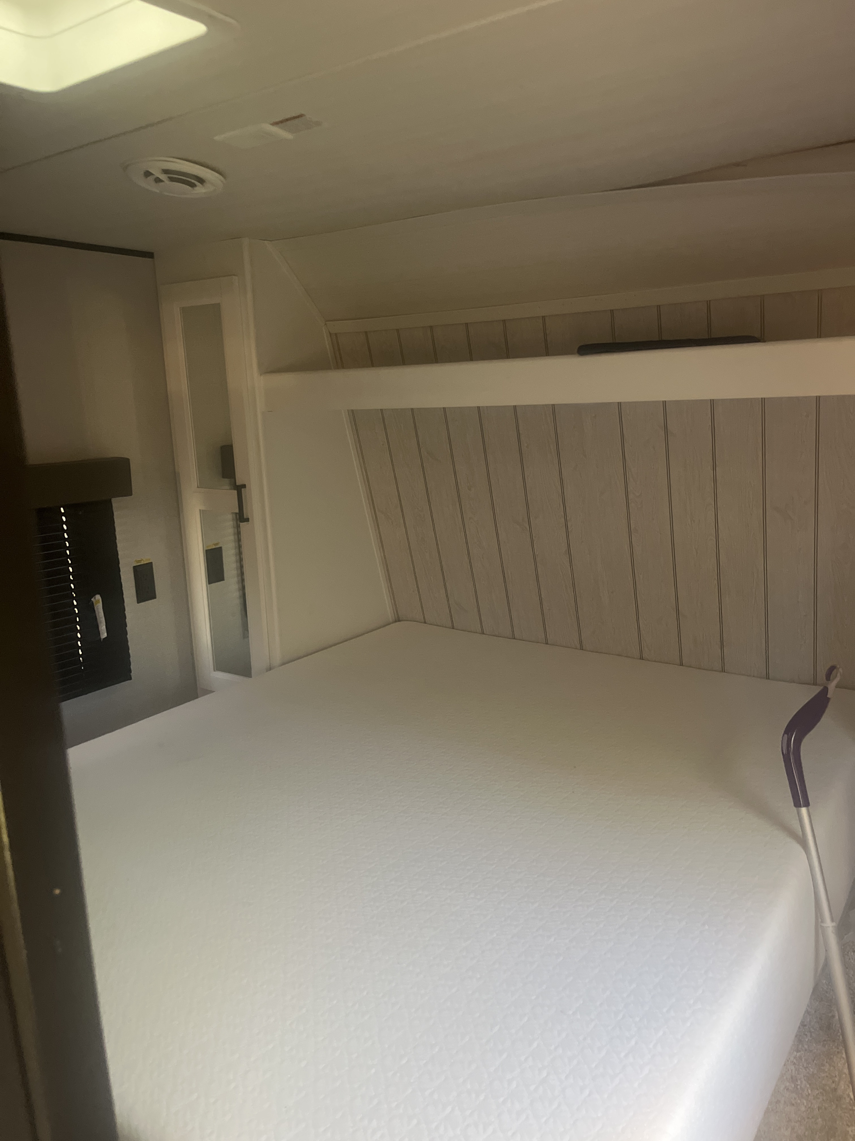 Bright RV rental bedroom interior features a crisp white bed, wood-paneled headboard, and practical overhead storage.. Keystone RV Hideout 2022