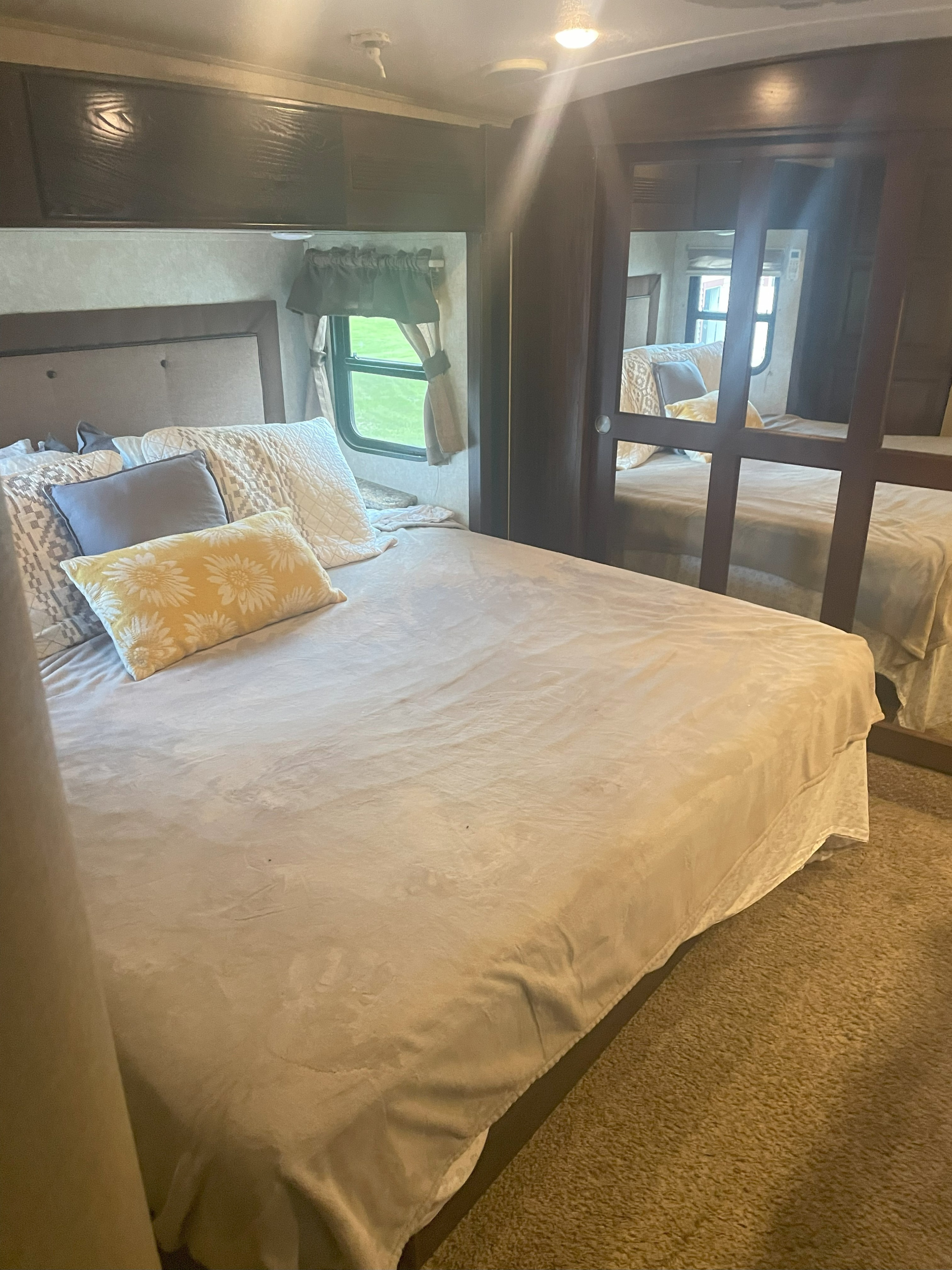 Cozy RV rental bedroom featuring a queen bed with decorative pillows, ample storage in overhead cabinets, and a mirrored wardrobe for comfort.. Keystone RV Montana Mountaineer 2015