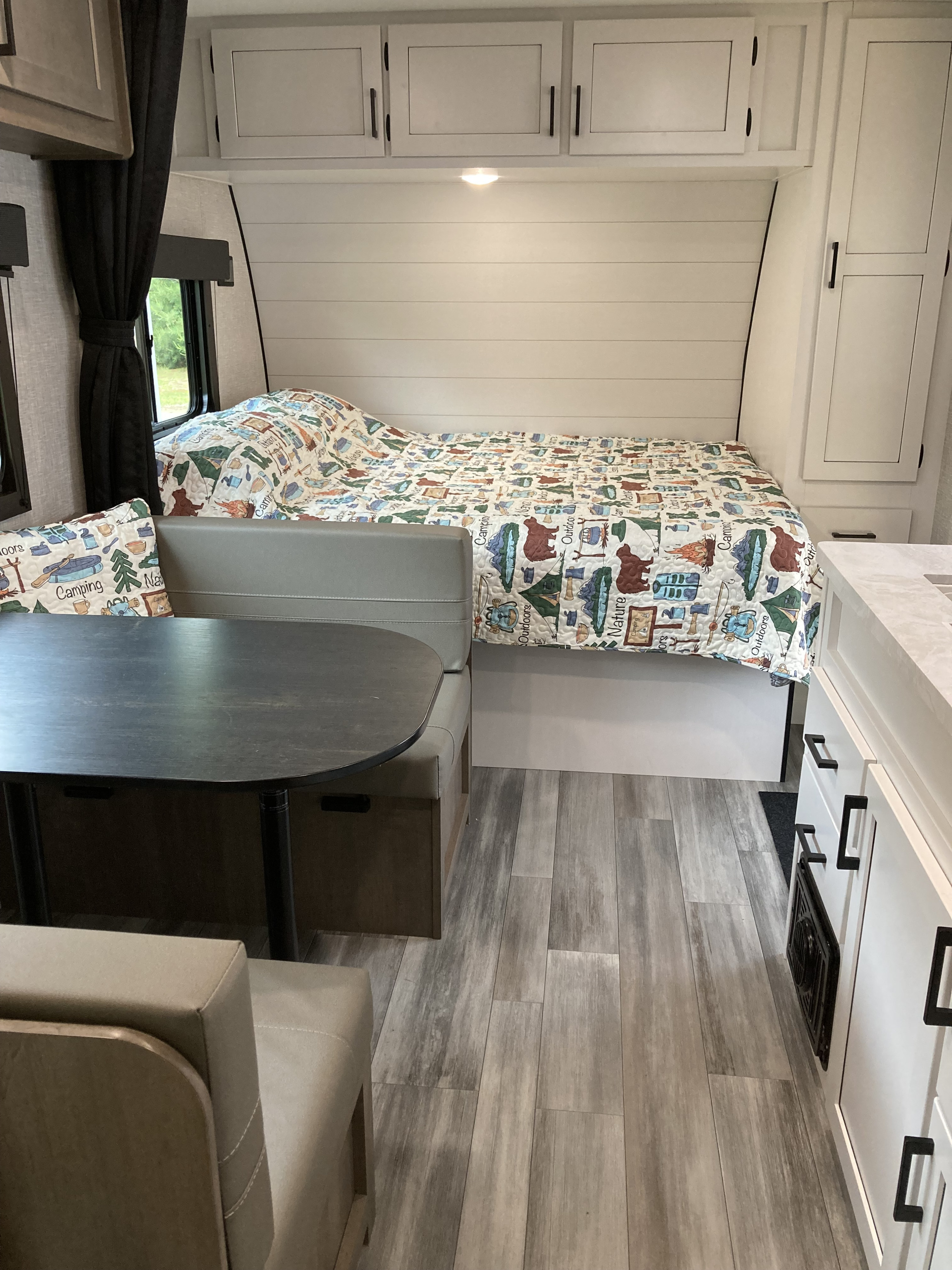Cozy RV rental interior showcasing a bed with a camping-themed quilt, dining area, and overhead storage cabinets.. Highland Ridge RV Open Range 2024