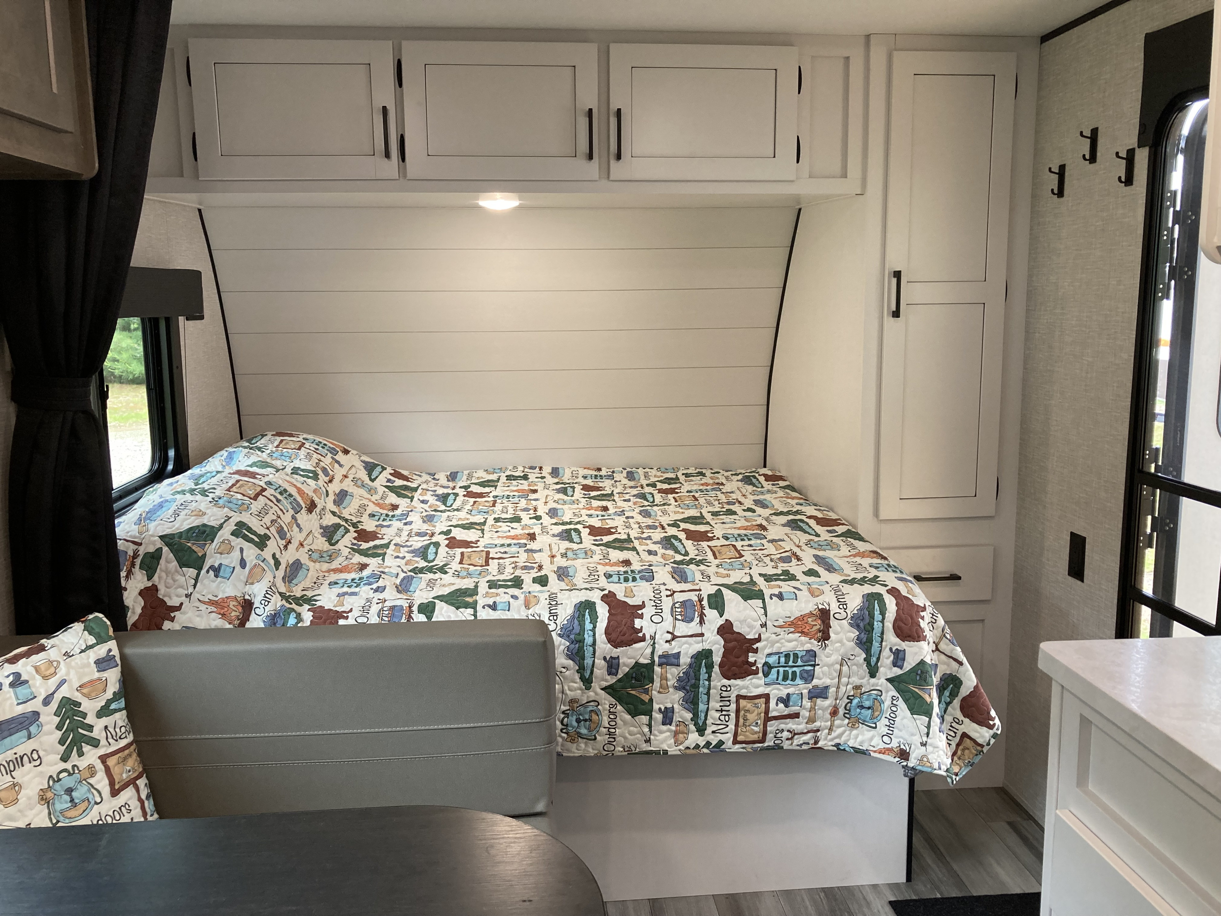 Cozy RV rental interior featuring a comfortable bed with a camping-themed quilt, overhead cabinets, and a dinette area.. Highland Ridge RV Open Range 2024
