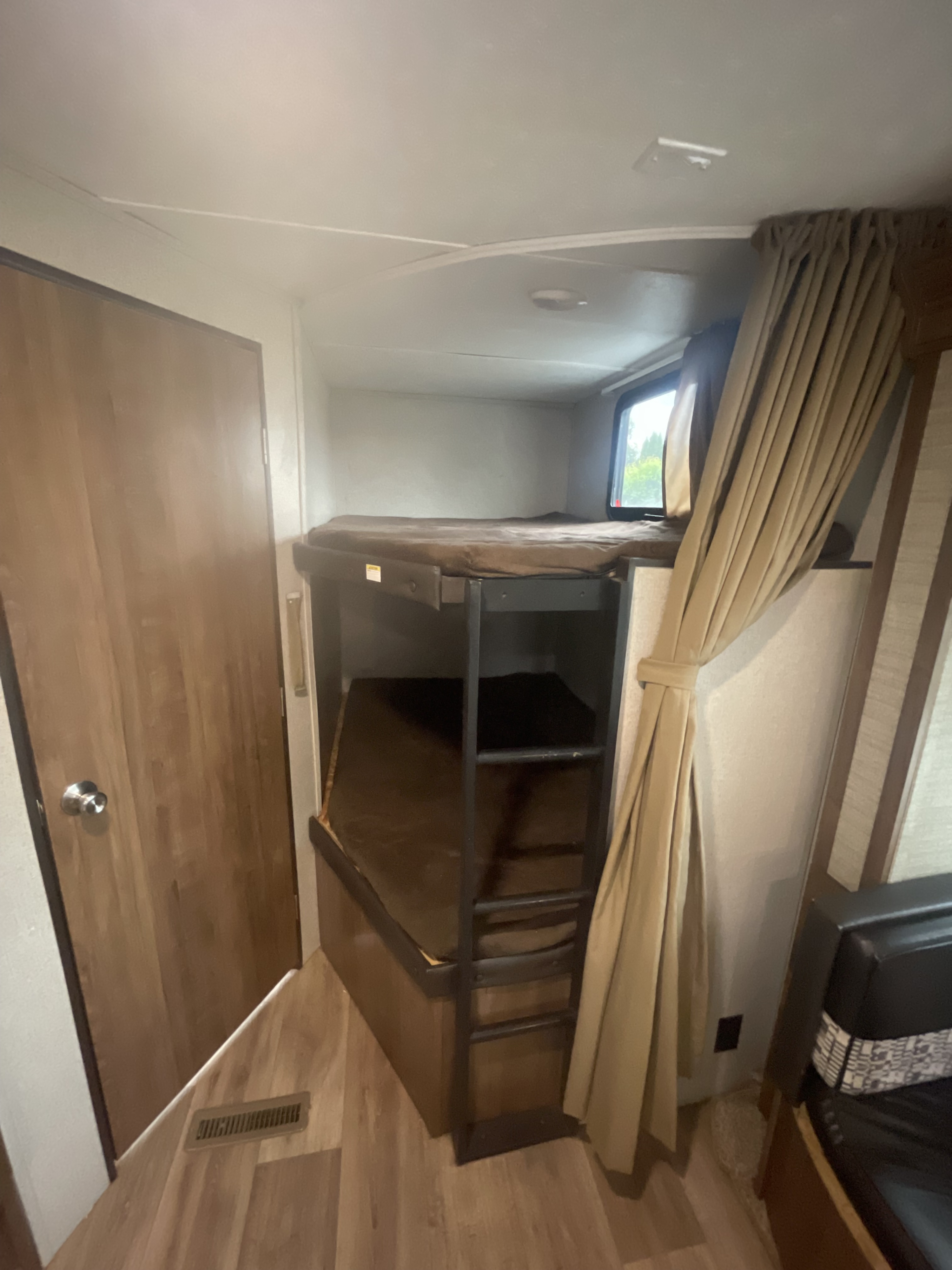 Comfortable bunk beds within an rv rental, showing a window, wooden door, and light interior, perfect for travelers.. Keystone RV Aspen Trail 2019