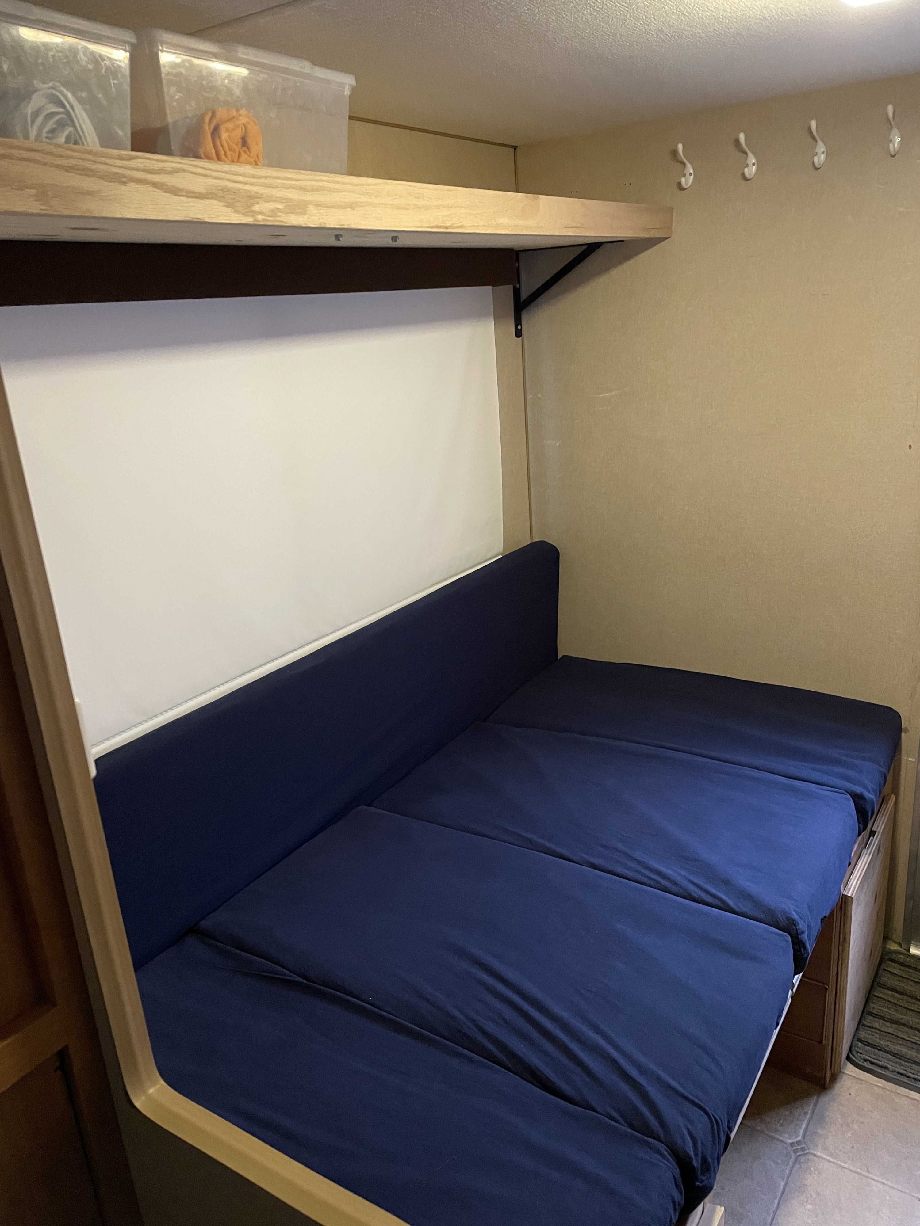 An rv rental interior featuring a blue upholstered bench that converts to a bed, overhead shelf storage, and wall hooks.. Gmc Sierra 2007