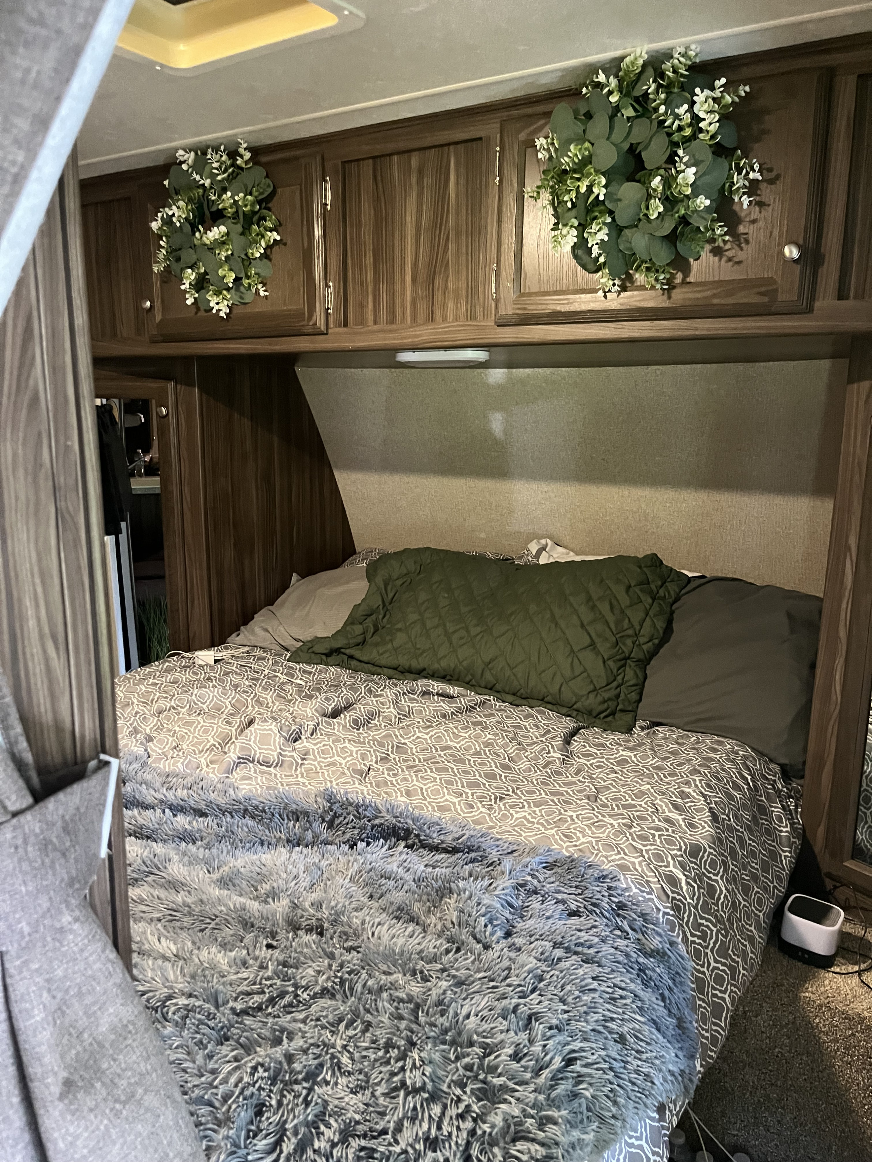 Cozy RV rental bedroom with a comfy grey bed, green pillows/decor, and overhead wood cabinets.. Coachmen Apex Ultra-Lite 28LE 2019
