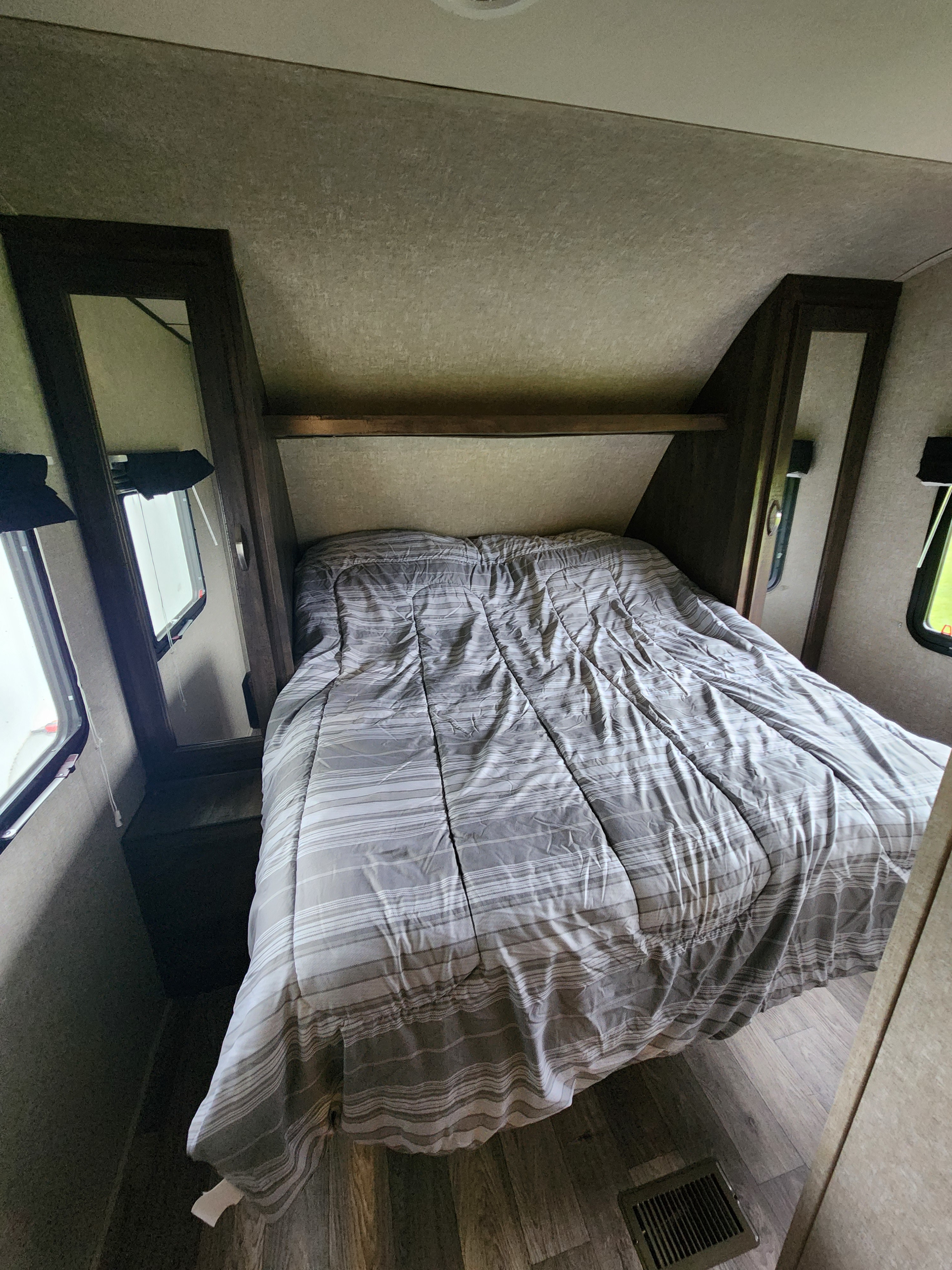 Cozy RV rental bedroom with a striped bed, side windows, and mirrored cabinets, offering compact comfort.. Forest River Vibe Extreme Lite 2018