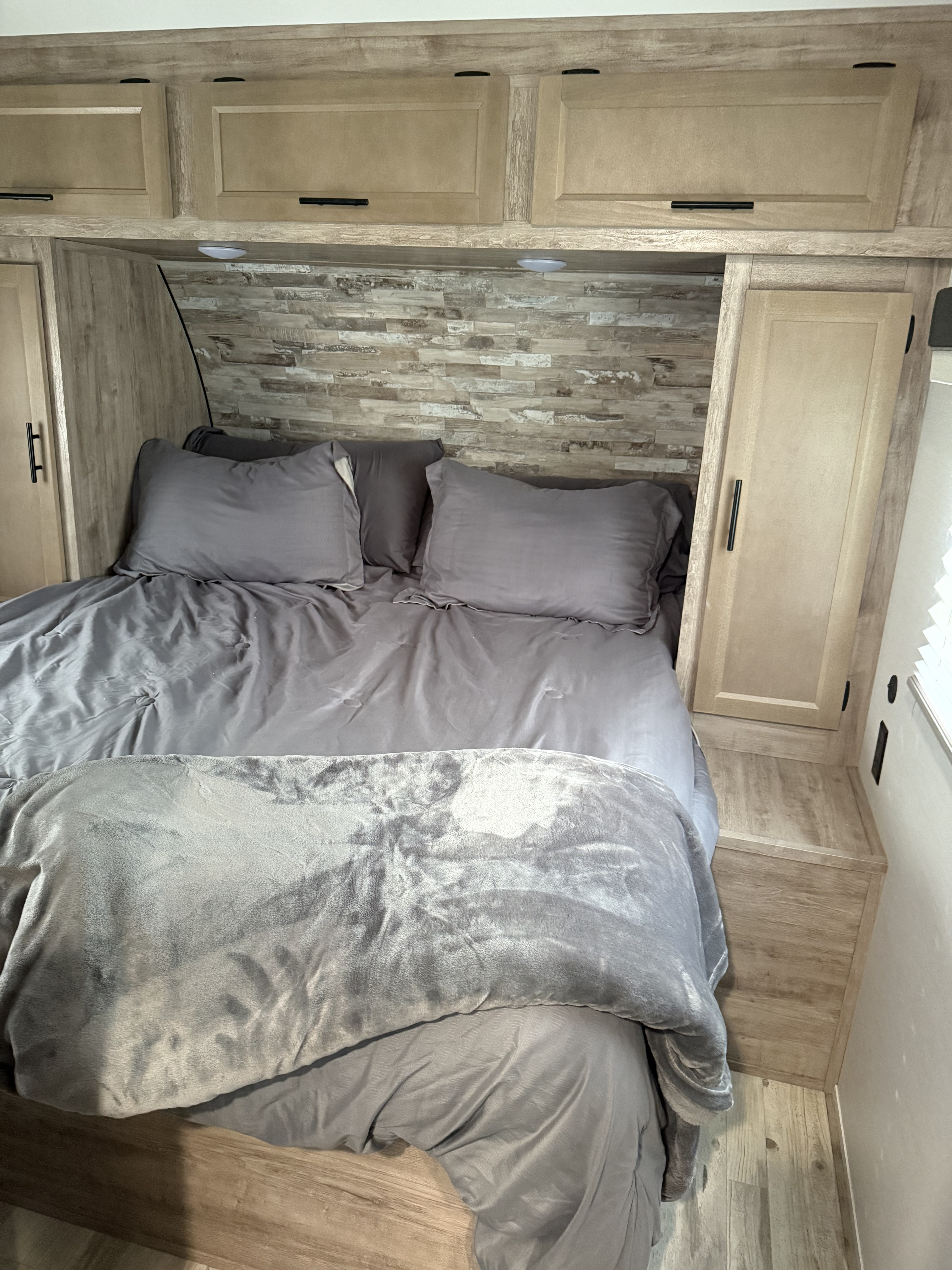 Experience comfort in this RV rental bedroom: gray bed, fuzzy blanket, overhead storage, and stylish wood-look interior.. Gulf Stream Kingsport Supreme 2024