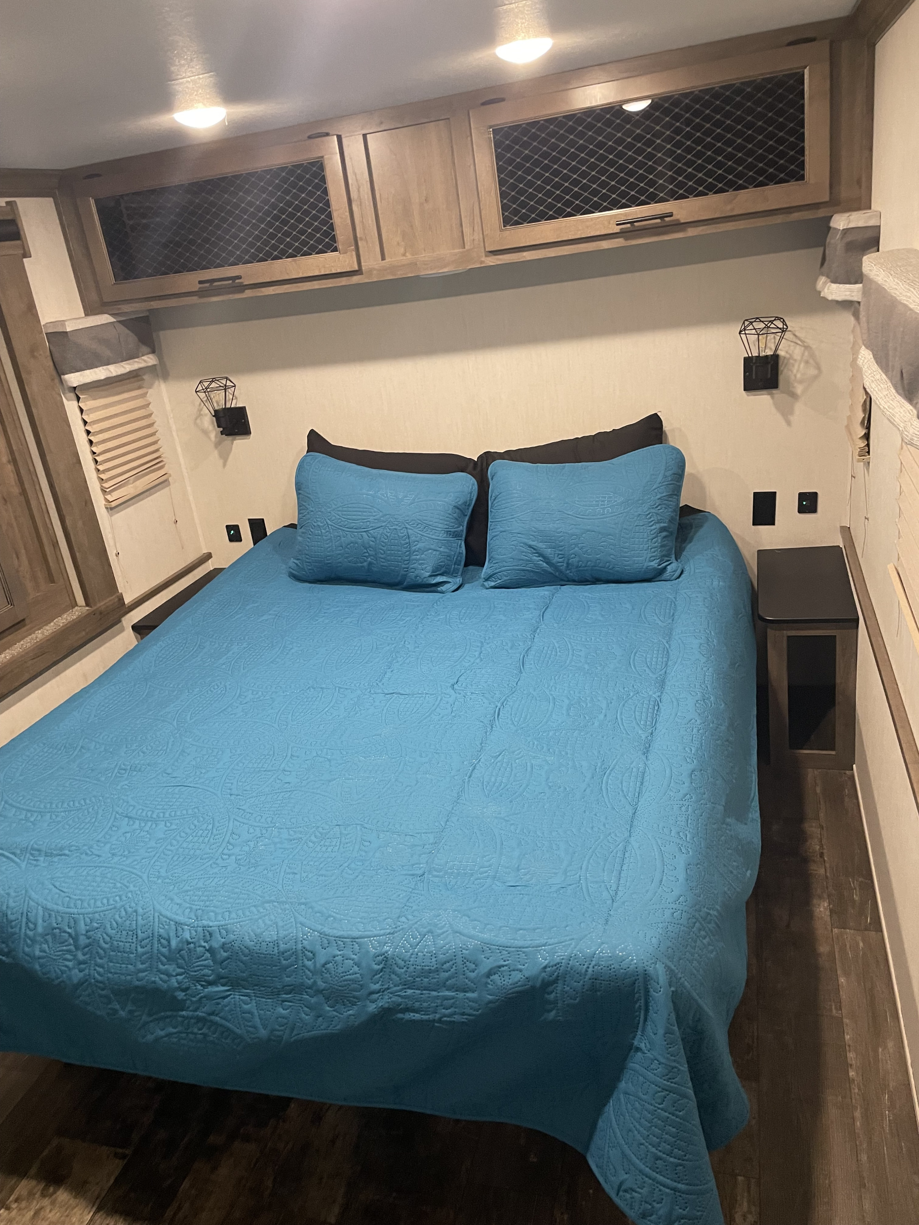 RV rental interior: a neatly made bed with blue linens, overhead cabinets, and compact bedside tables.. Foreest River Sabre 2022
