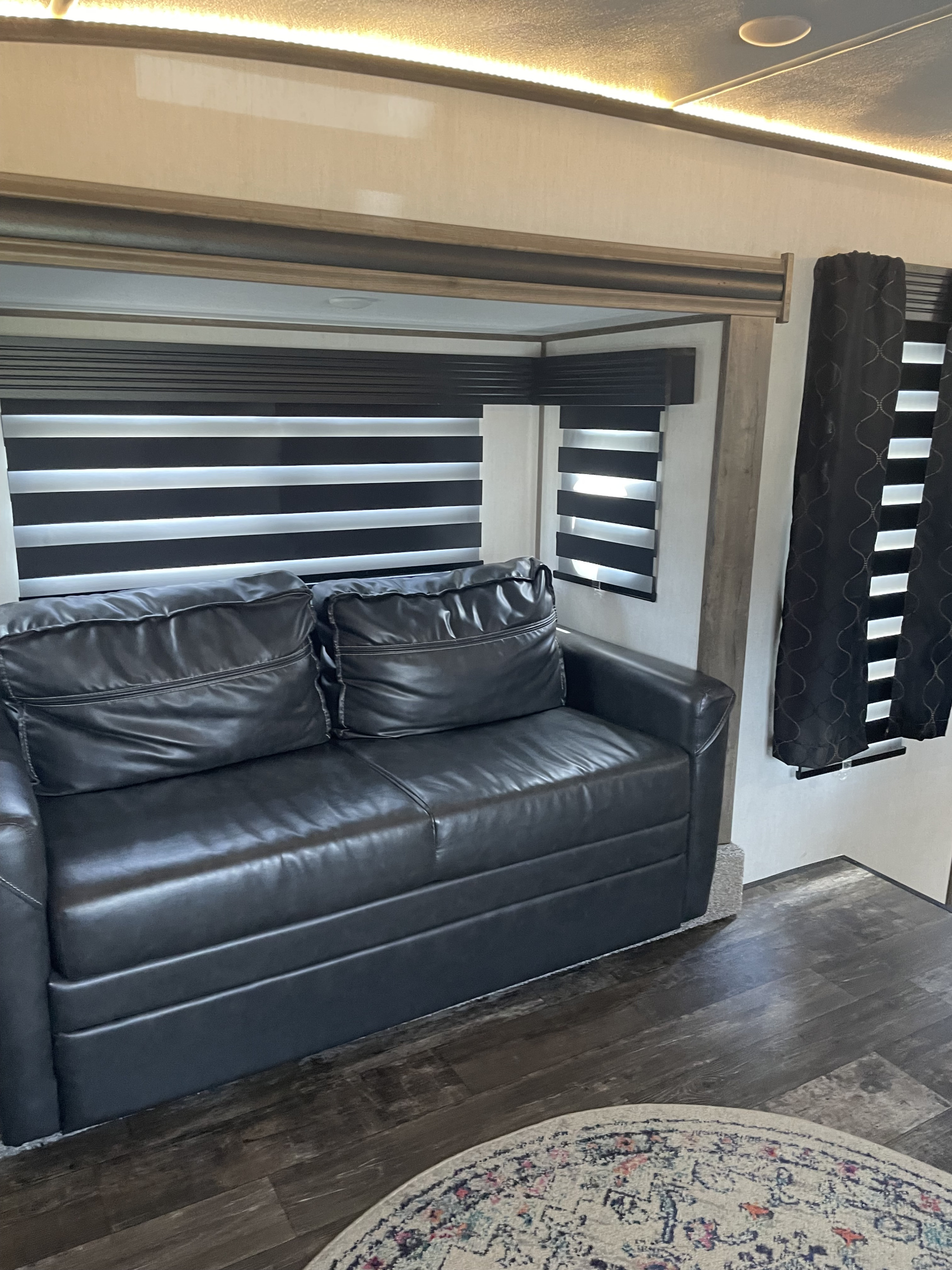 Spacious RV rental living area featuring a dark leather sofa, striped window blinds, and modern LED ceiling lights.. Foreest River Sabre 2022