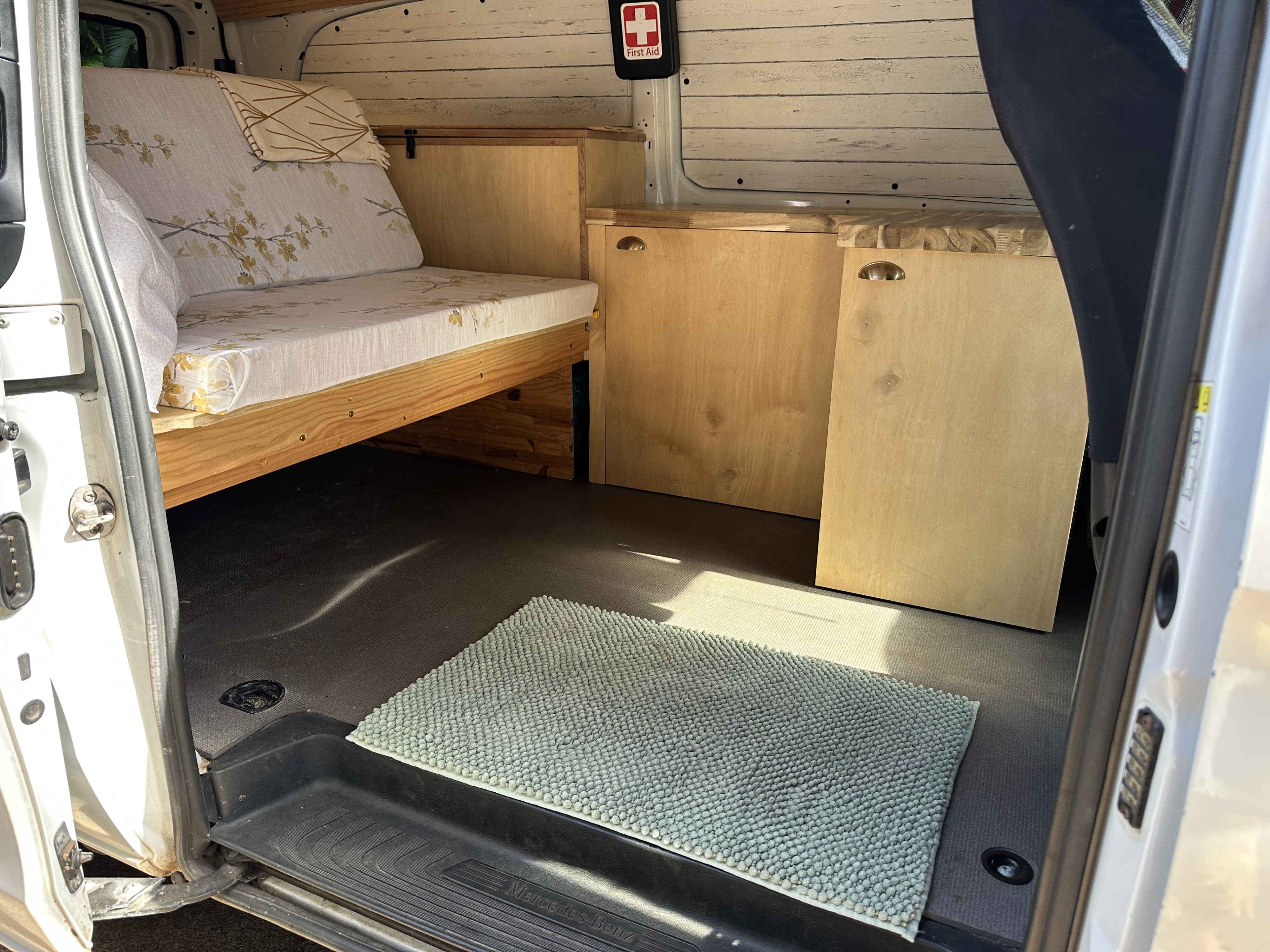 Inside a well-appointed Mercedes-Benz RV rental. Features custom bed/couch, wooden cabinets, and a neat interior.. Mercedes-Benz Metris 2020