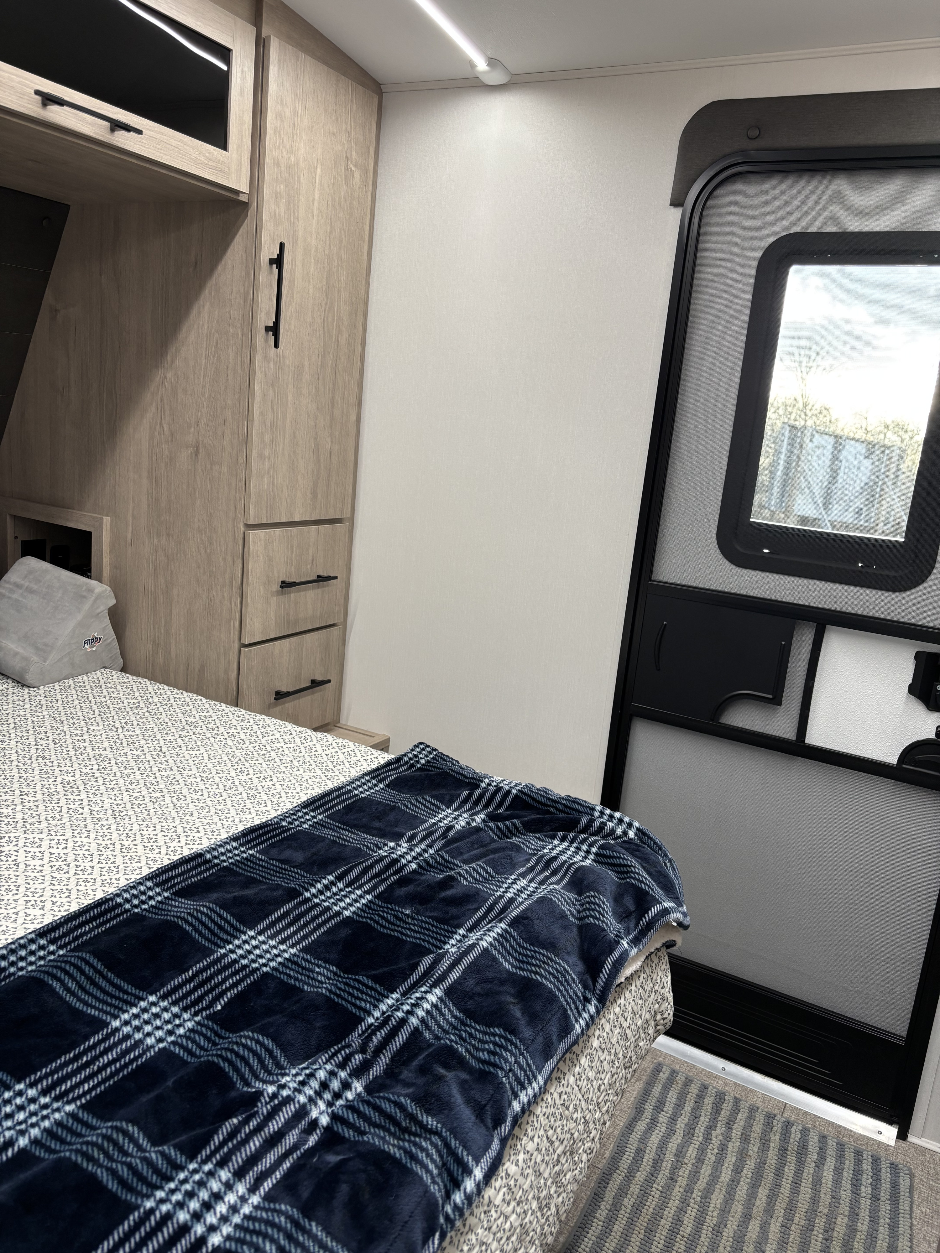 Comfortable rv rental interior featuring a bed with a cozy plaid blanket, wood cabinets, and an entry screen door.. Imagine 2300MK 2025