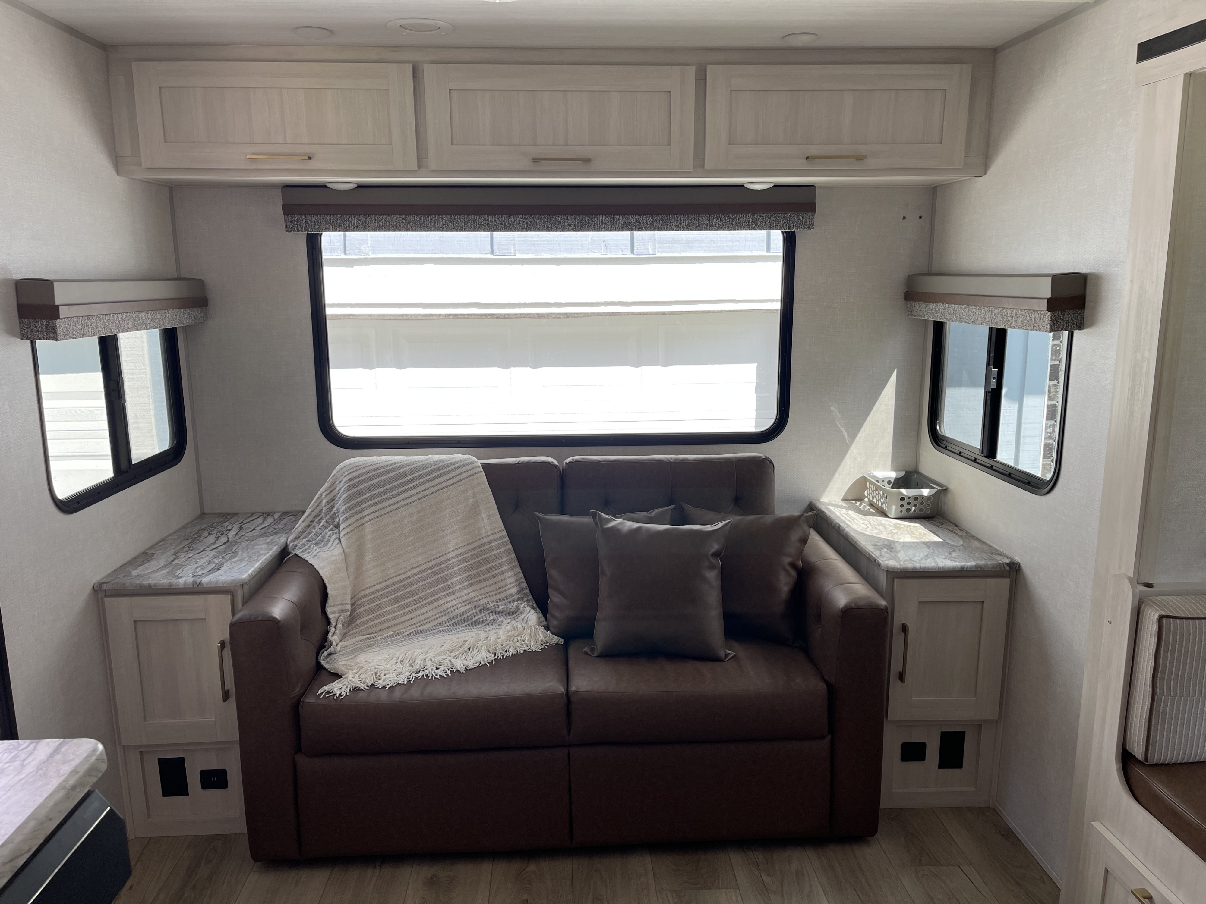 Cozy RV rental living space with brown sofa, light cabinets, and large windows, perfect for travel.. Forest River Grand Surveyor 2024