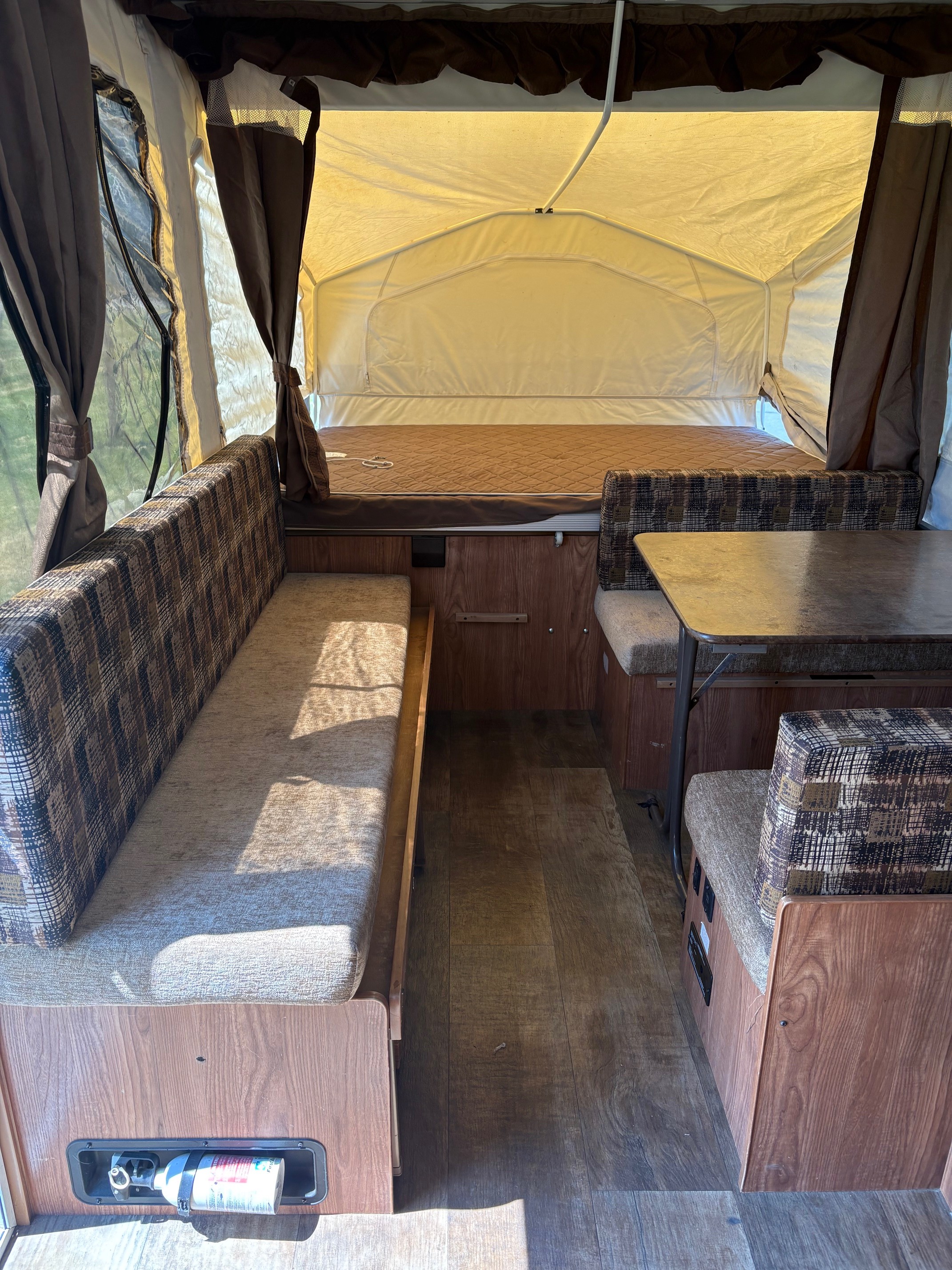 Interior of an RV rental pop-up camper, showing bench seating, a dinette with table, and a rear bed area.. Rockwood Freedom 2280 BH 2016