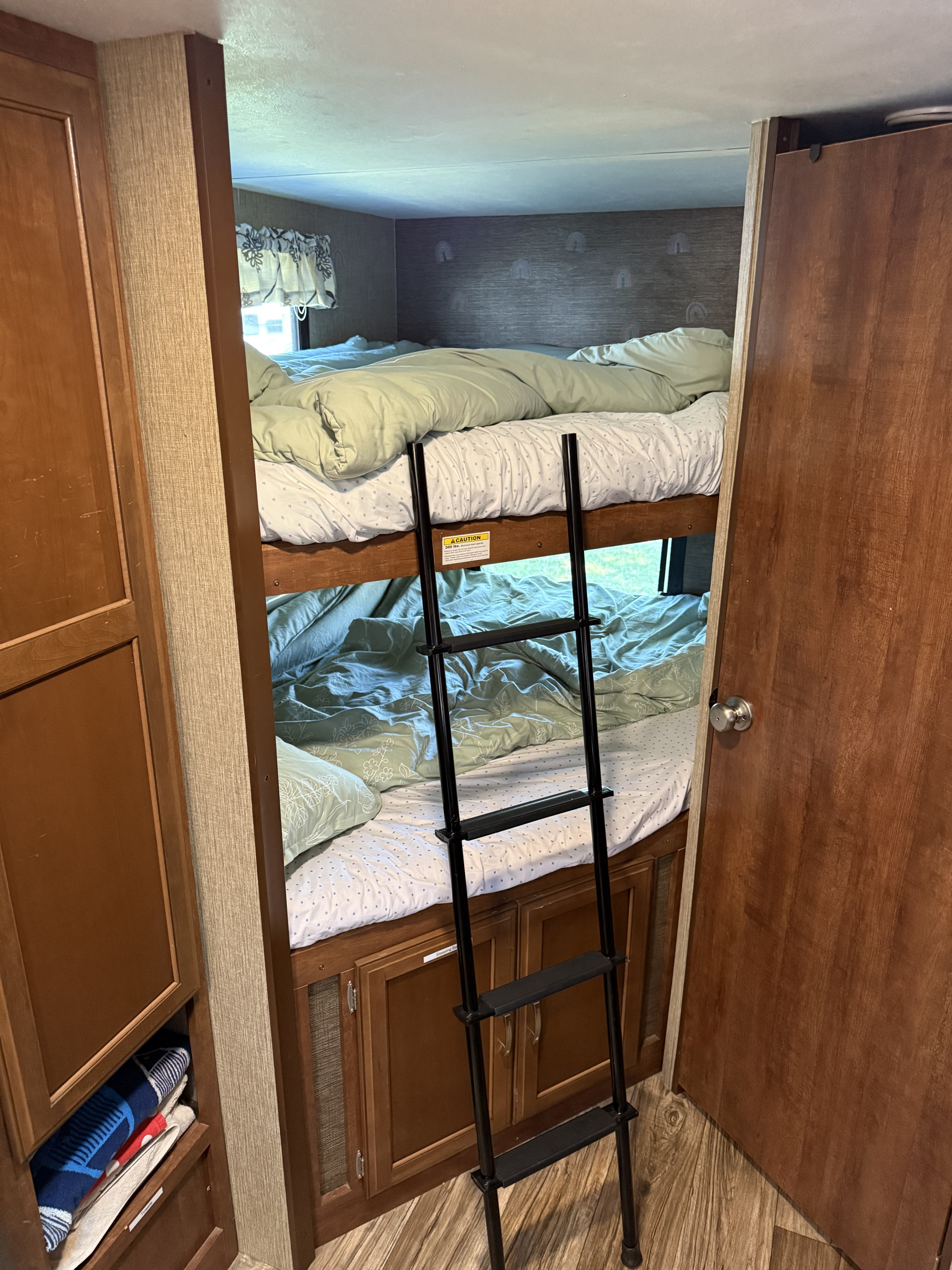 Cozy RV rental bunk beds with ladder, made up with light green bedding. Features compact sleeping quarters for travel.. Keystone RV Passport Grand Touring 2017