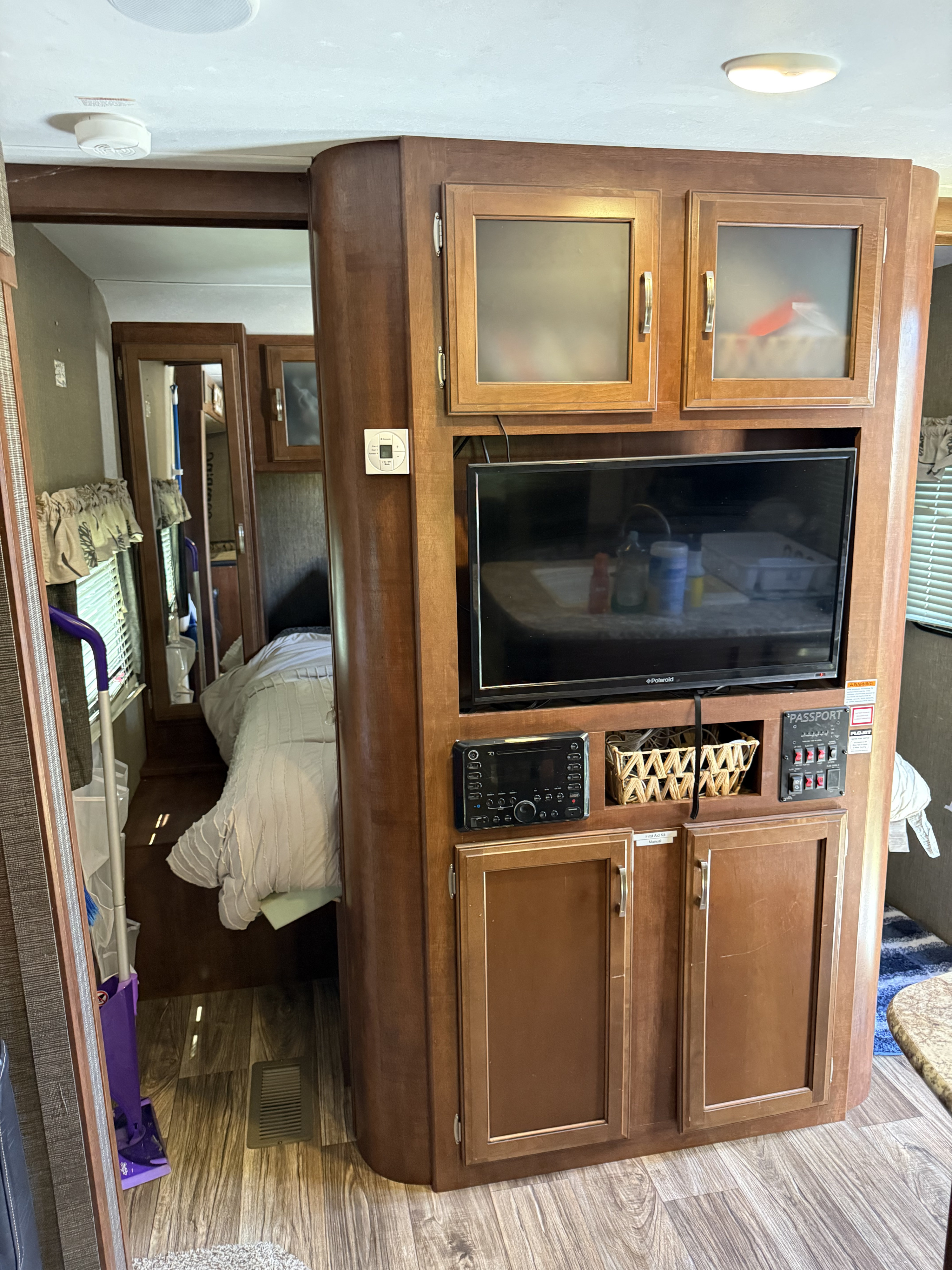 RV rental interior featuring a central entertainment unit with TV, stereo, and controls, opening to a cozy bedroom area.. Keystone RV Passport Grand Touring 2017