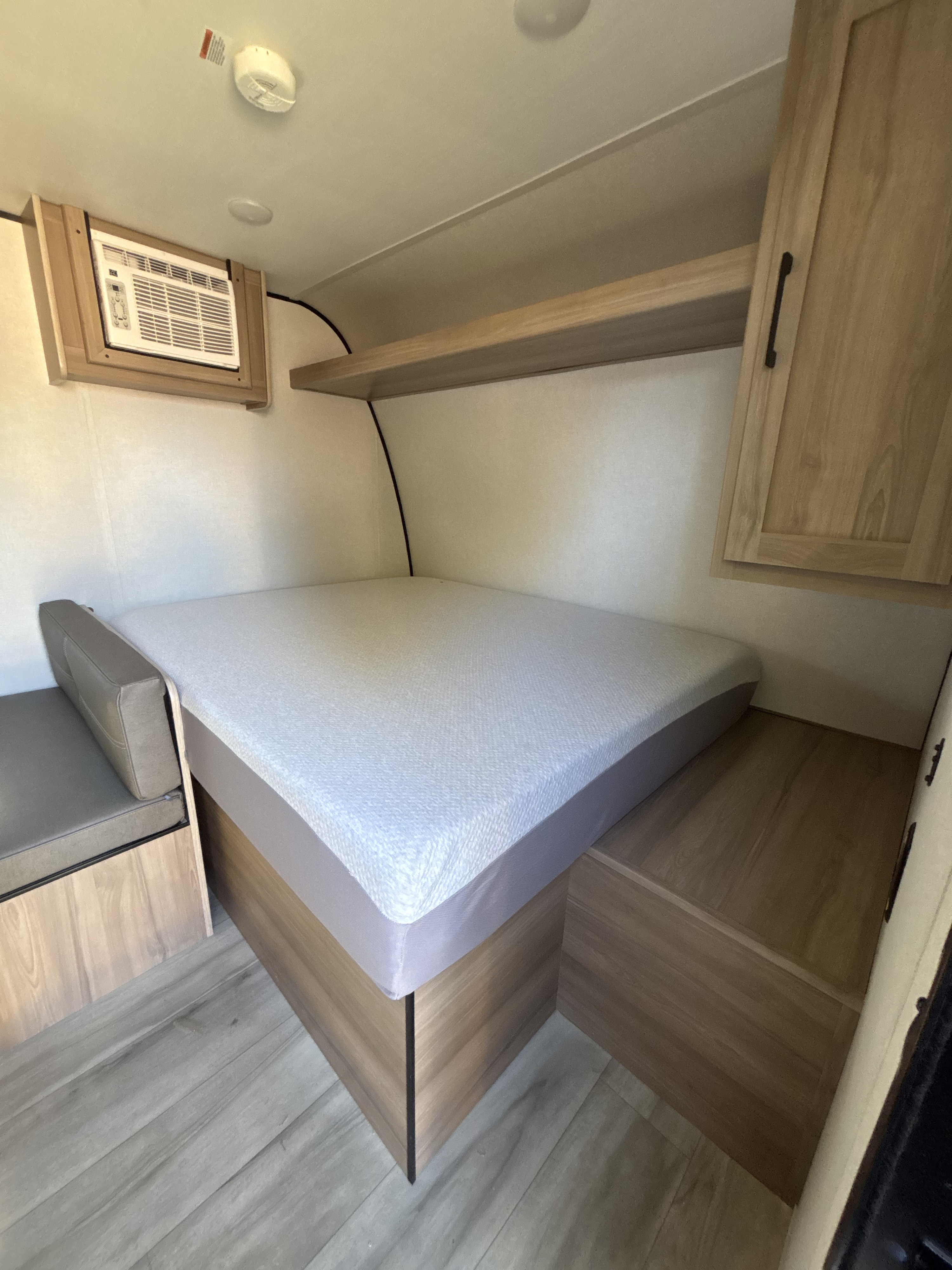 Cozy RV rental bedroom featuring a comfortable bed, AC unit, bench seating, and ample overhead storage for your travels.. Keystone Coleman 17b 2025