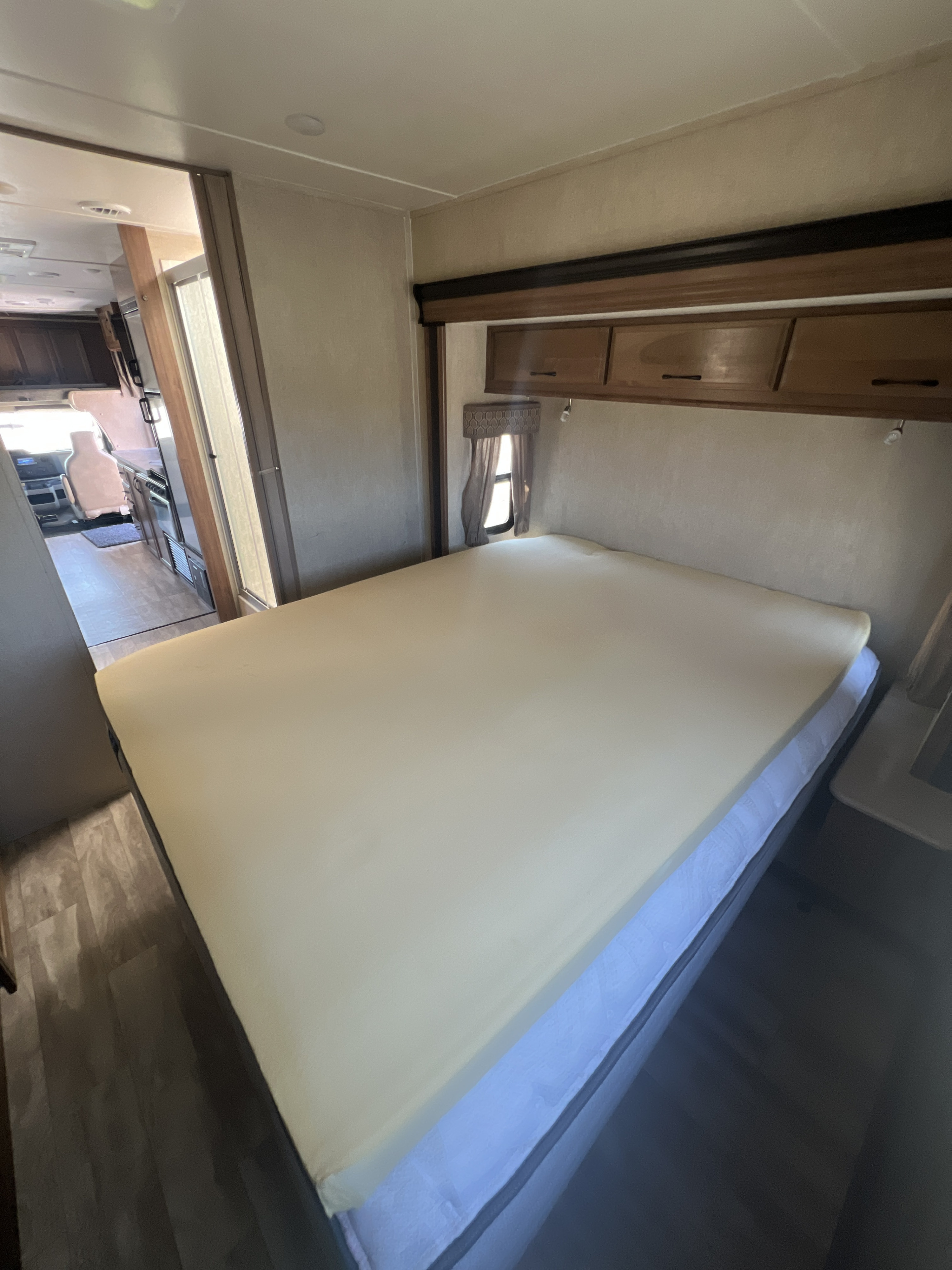 Inside an RV rental: a cozy bedroom with a large bed topped with foam, overhead storage, and a glimpse of the kitchen area.. Gulf Stream Conquest 2019