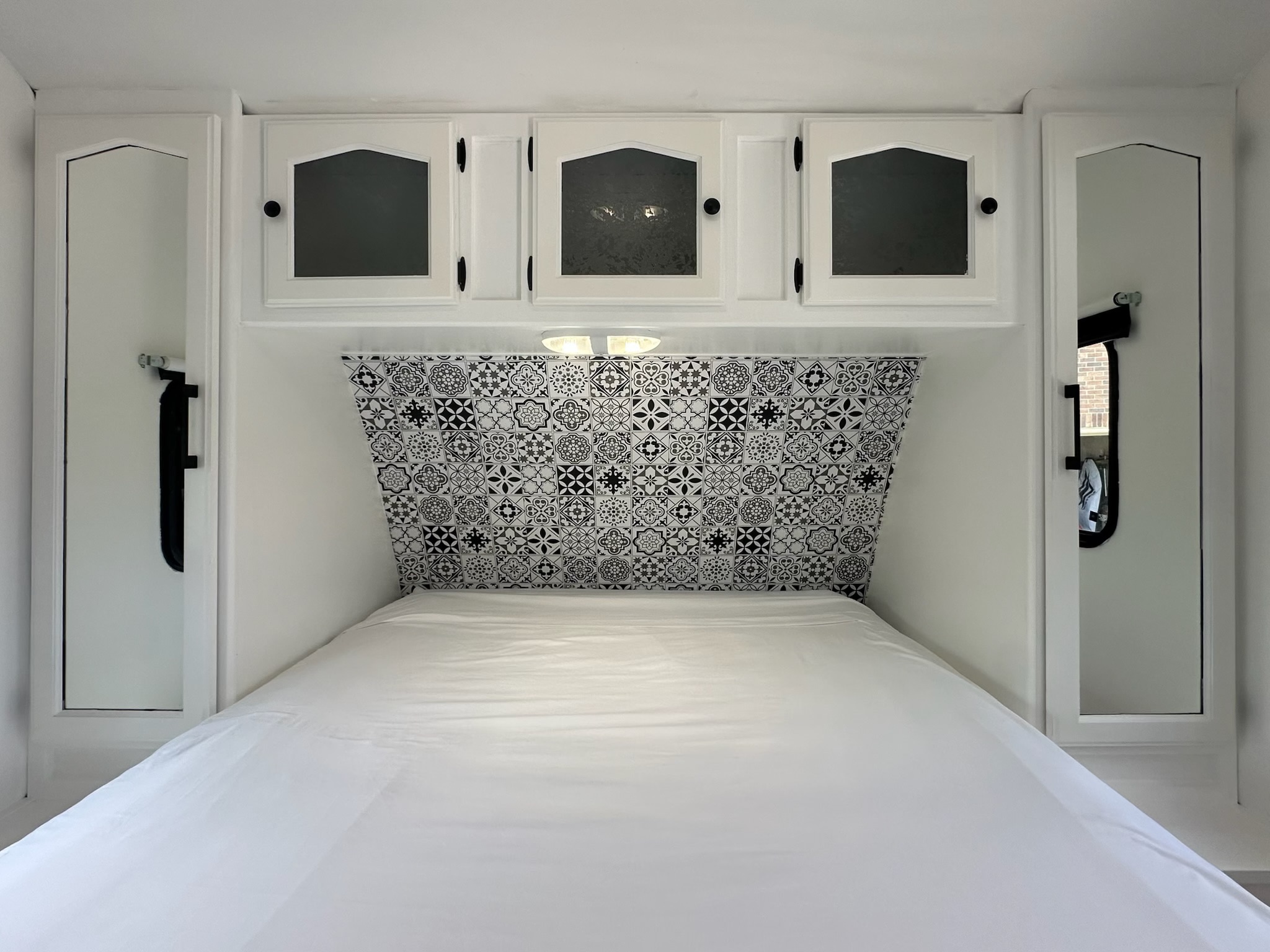 Bright RV rental bedroom, featuring a white bed, patterned headboard, and overhead/side storage cabinets.. Keystone RV Passport GT 2011