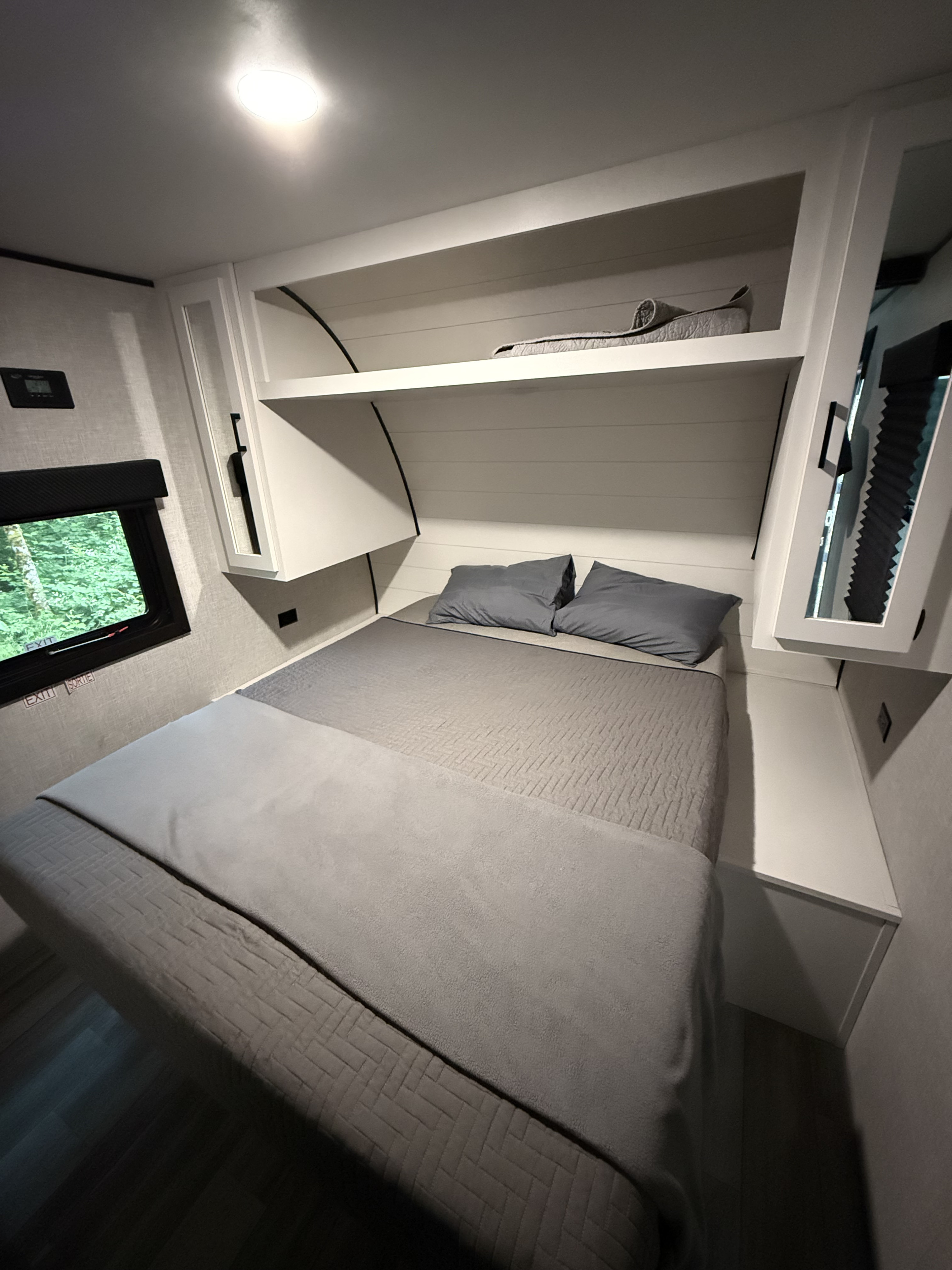 Cozy compact RV rental bedroom interior with gray bed, built-in storage, and window view of greenery.. Highland Ridge RV Open Range 2024