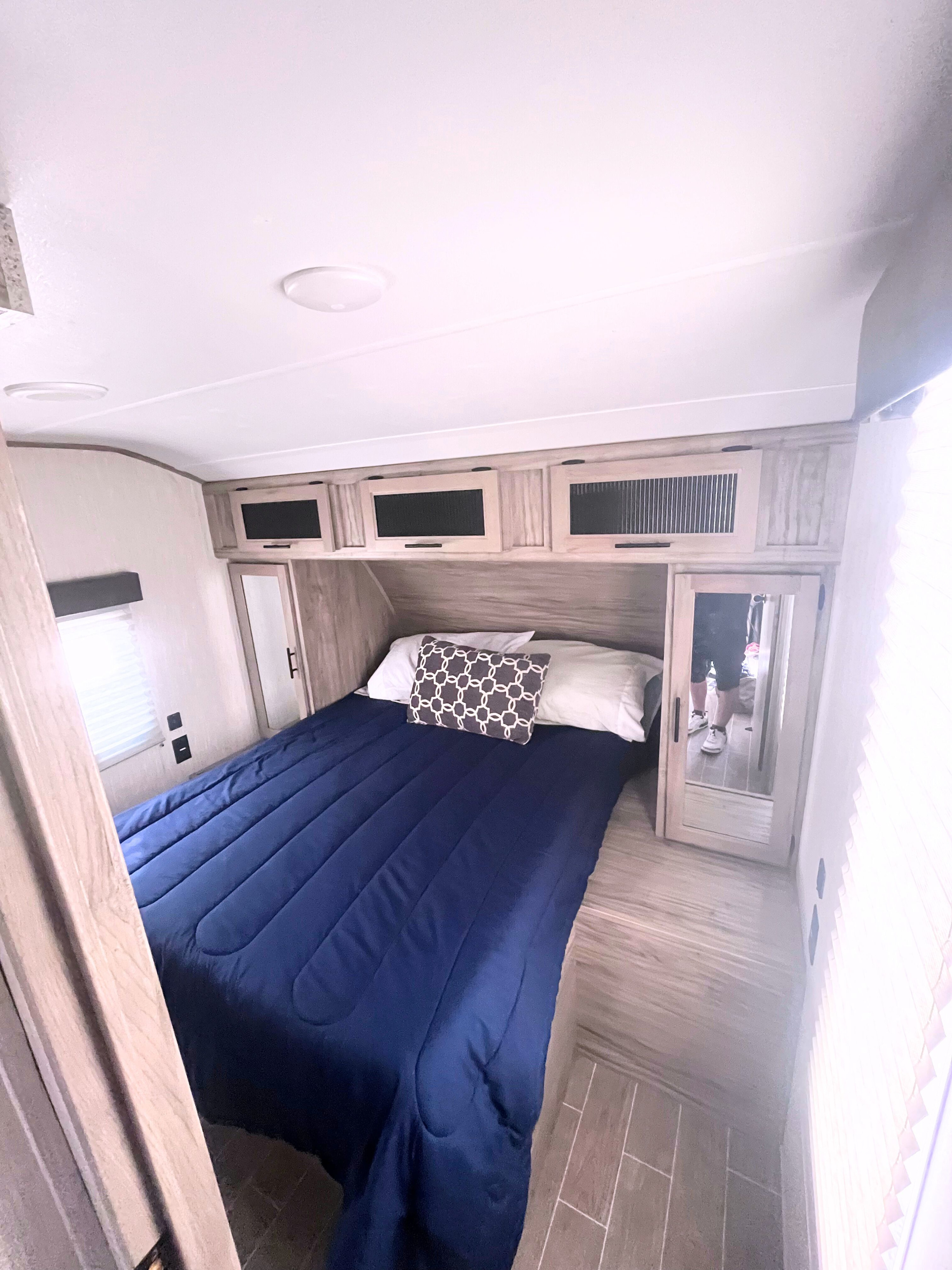 RV rental bedroom interior featuring a comfortable bed with blue comforter, overhead cabinets, and mirrored wardrobes.. Forest River Cherokee Alpha Wolf 2021